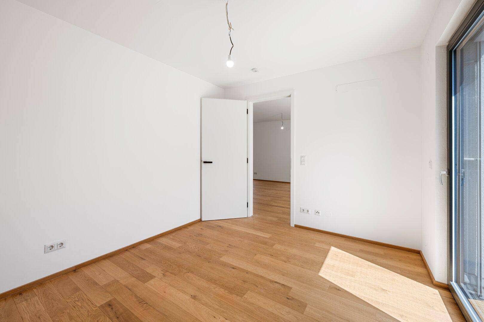 Helles Schlafzimmer mit Eichenparkettboden und Zugang zu einem weiteren Raum.