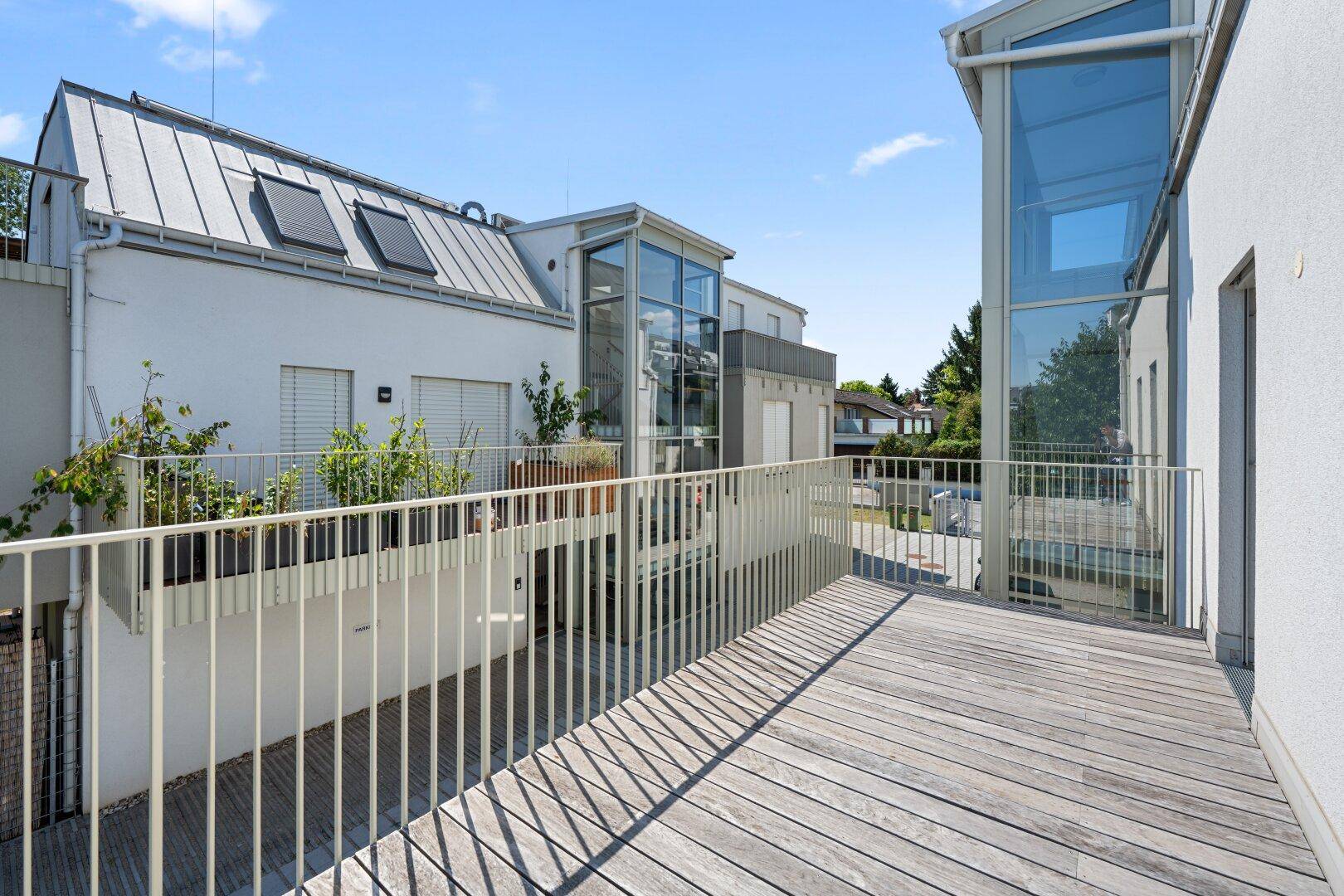 Große Holzterrasse mit Metallgeländer und Blick auf moderne Gebäude mit Glasfassaden.