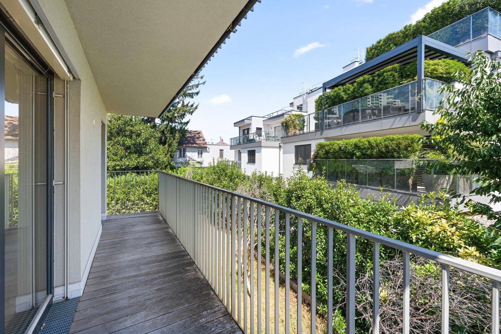 Balkon mit Holzboden und Blick auf moderne Gebäude mit begrünten Terrassen.