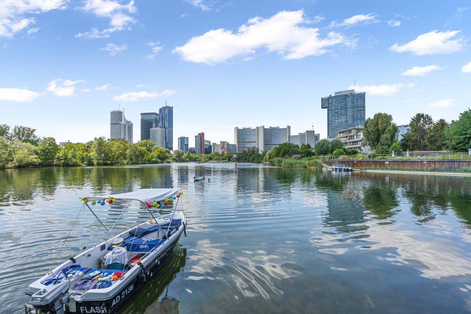 Panoramablick auf einen See mit Booten und die Skyline einer modernen Stadt im Hintergrund.