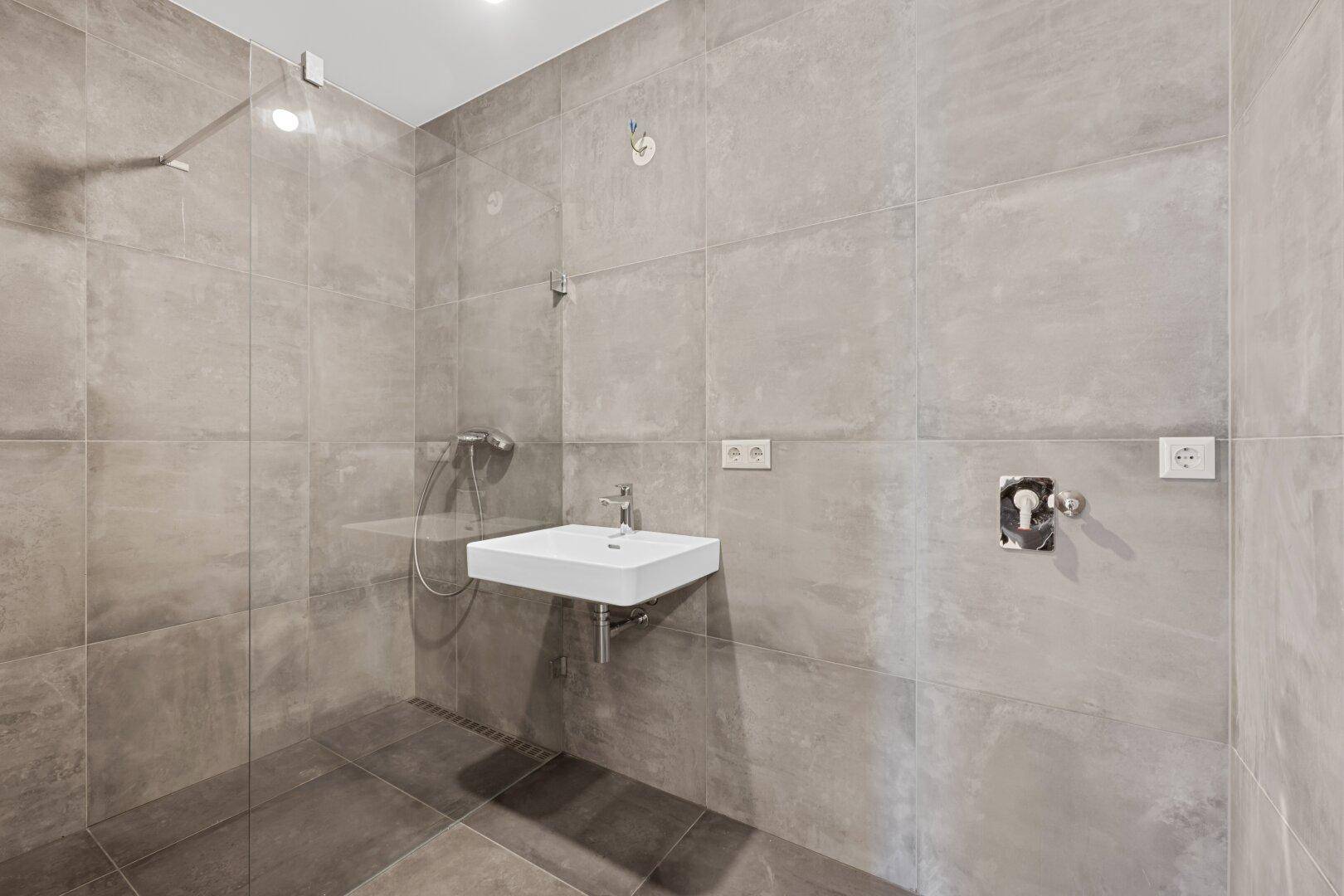Modernes Badezimmer mit grauen Fliesen, ebenerdiger Dusche und schwebendem Waschbecken.