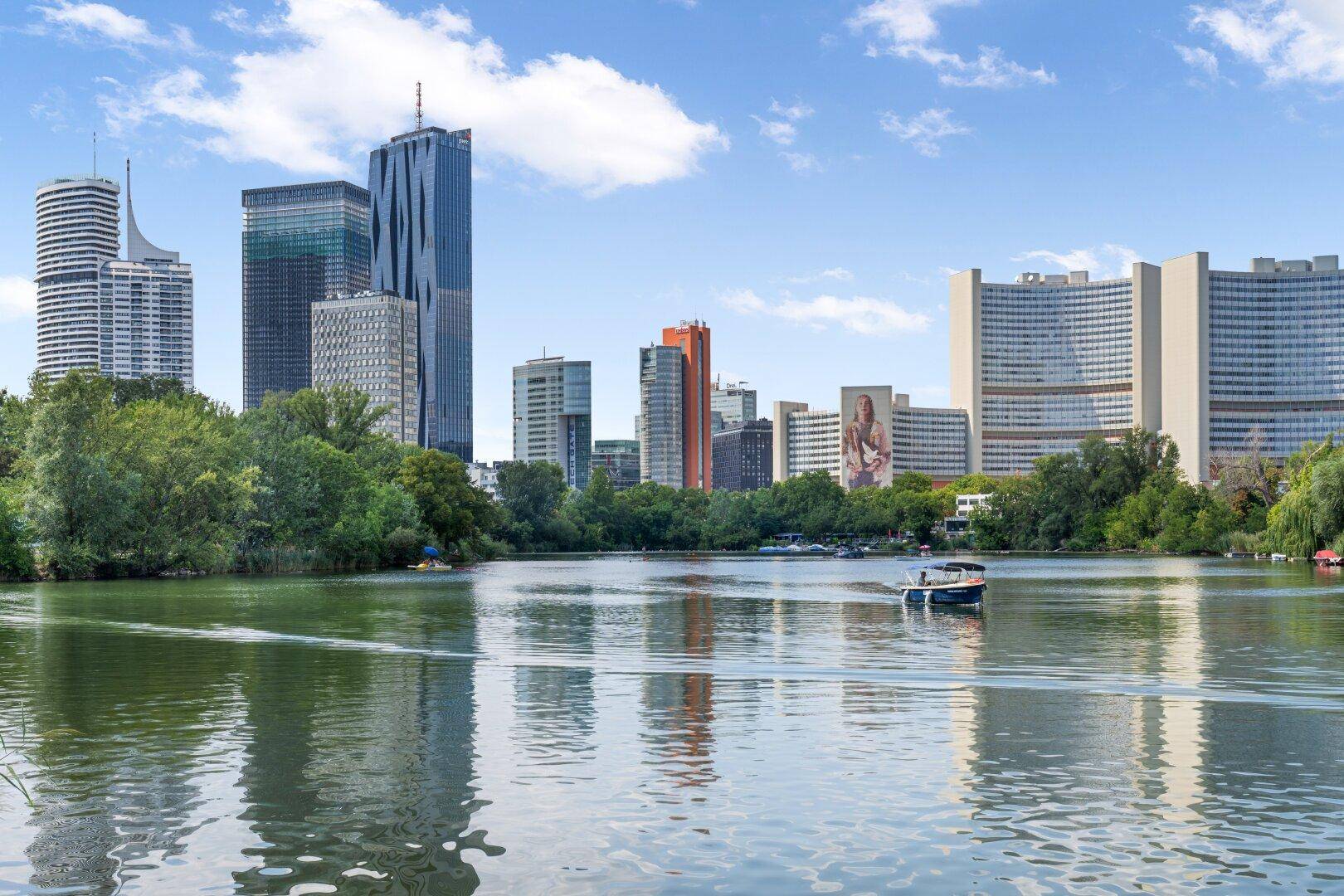 Panoramablick auf einen See mit Booten und die Skyline einer modernen Stadt im Hintergrund.