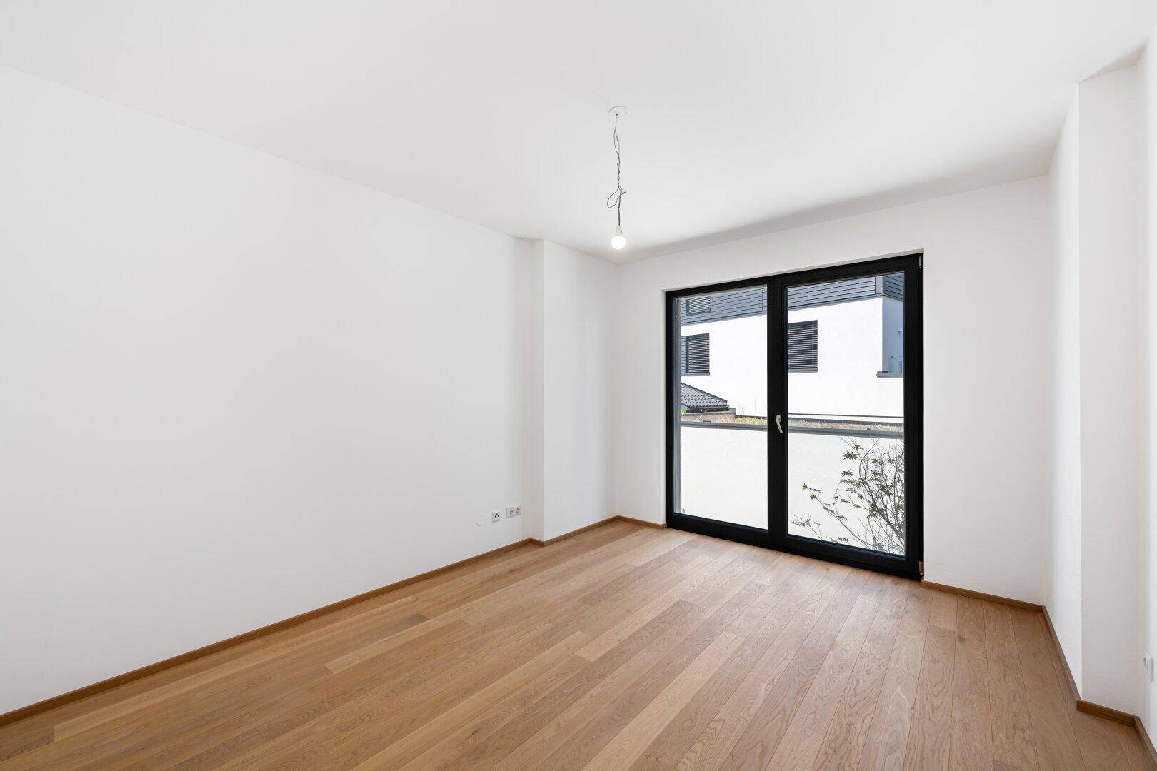 Helles Schlafzimmer mit Eichenparkettboden und großer Schiebetür, die viel Tageslicht hereinlässt.