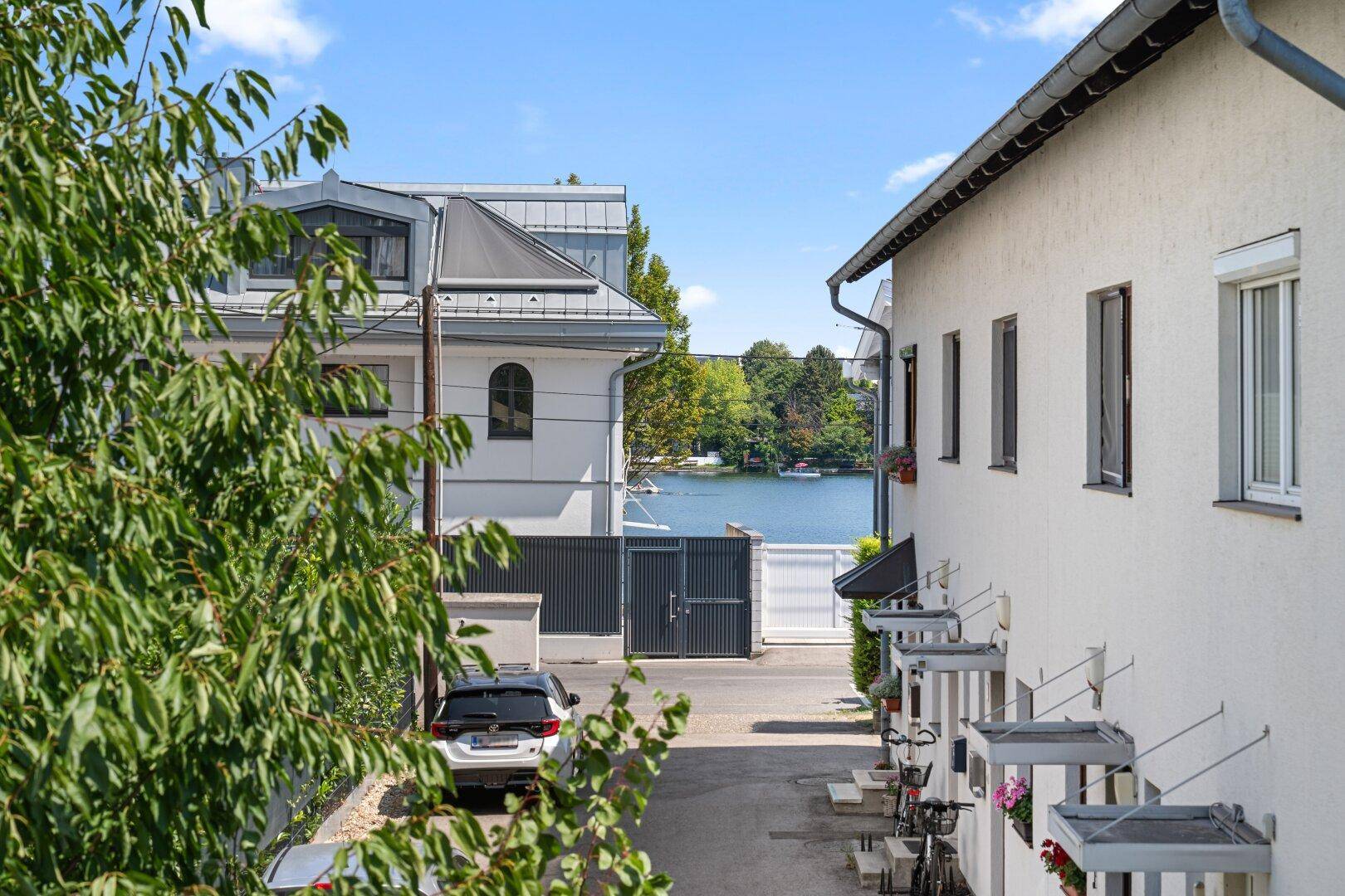 Blick zwischen Gebäuden hindurch auf den See und die gegenüberliegende Uferseite.