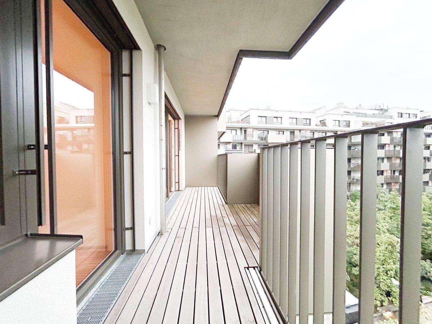 Geräumiger Balkon mit Holzboden und Blick auf die umliegenden Gebäude und Bäume.