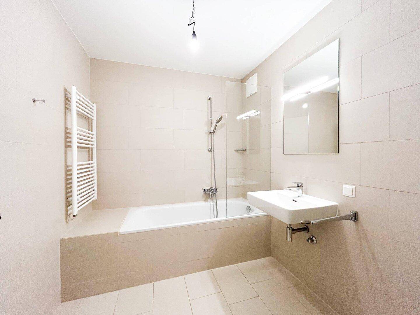 Modernes Badezimmer mit Badewanne, Duschvorrichtung und beheiztem Handtuchhalter.