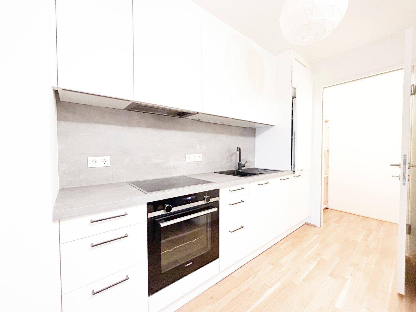Moderne Einbauküche mit weißen Fronten, Induktionskochfeld und integriertem Backofen.