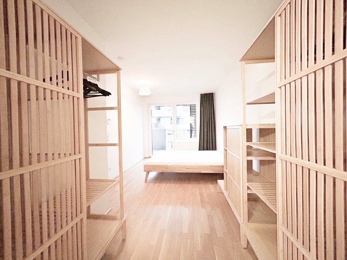 Schlafzimmer mit offenem Kleiderschranksystem aus Holz und hellem Parkettboden.