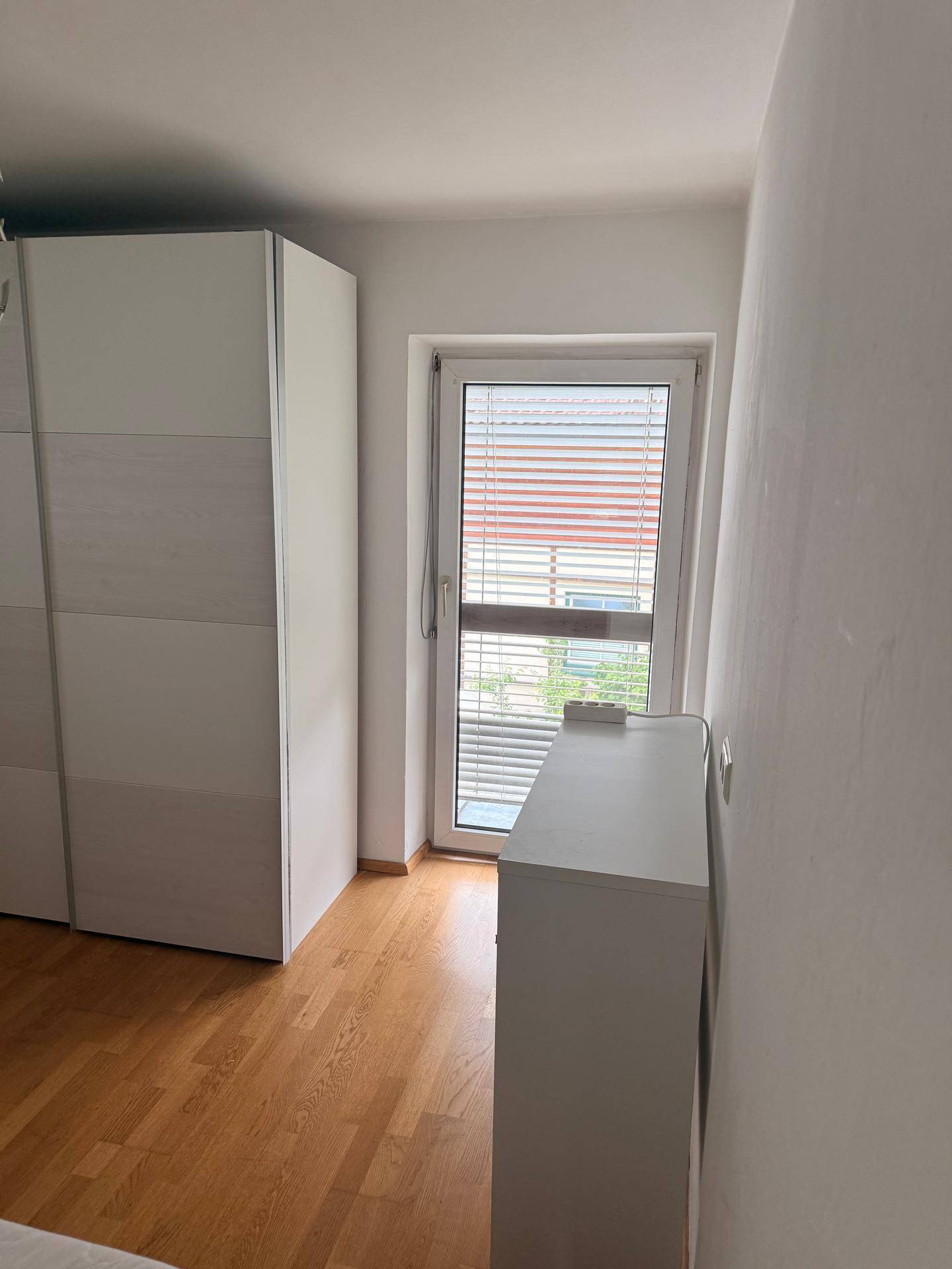Schlafzimmer mit großem Schiebetürenschrank, Kommode und Zugang zu einem französischen Balkon.