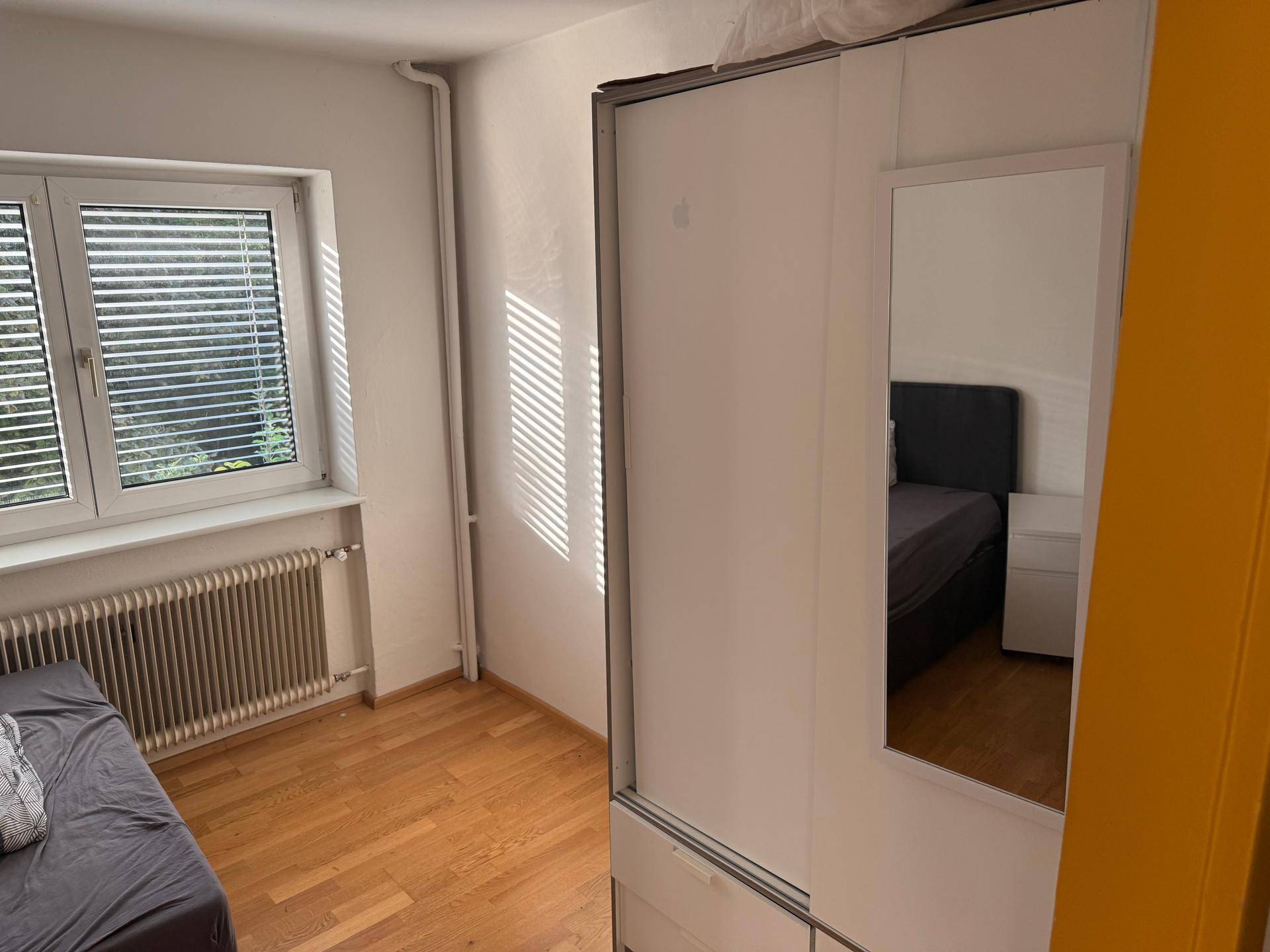 Helles Schlafzimmer mit Schiebetürenschrank, Fenster mit Jalousien und Holzboden.