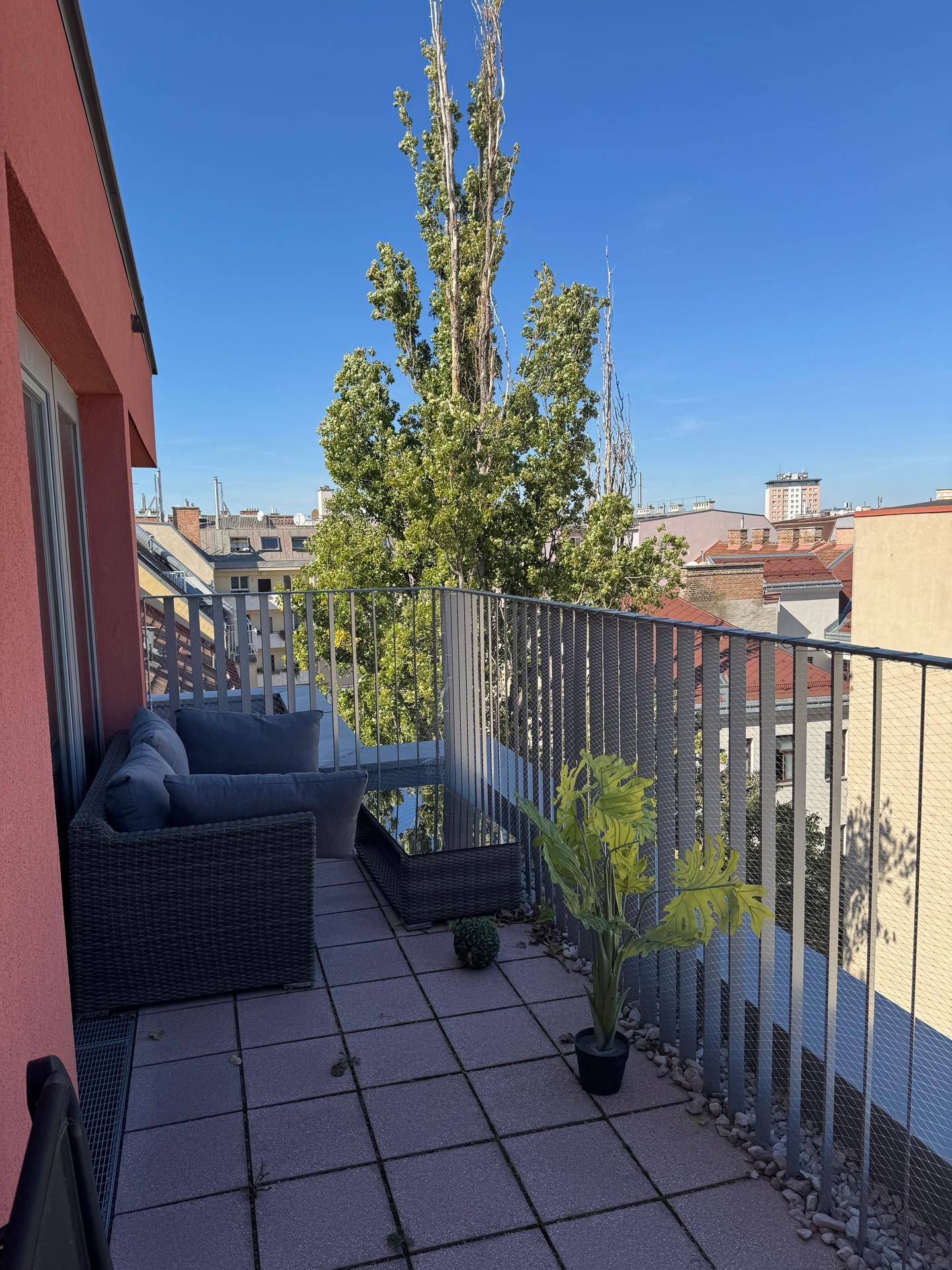 Sonniger Balkon mit Outdoor-Möbeln, Fliesenboden und Blick auf die Stadt.