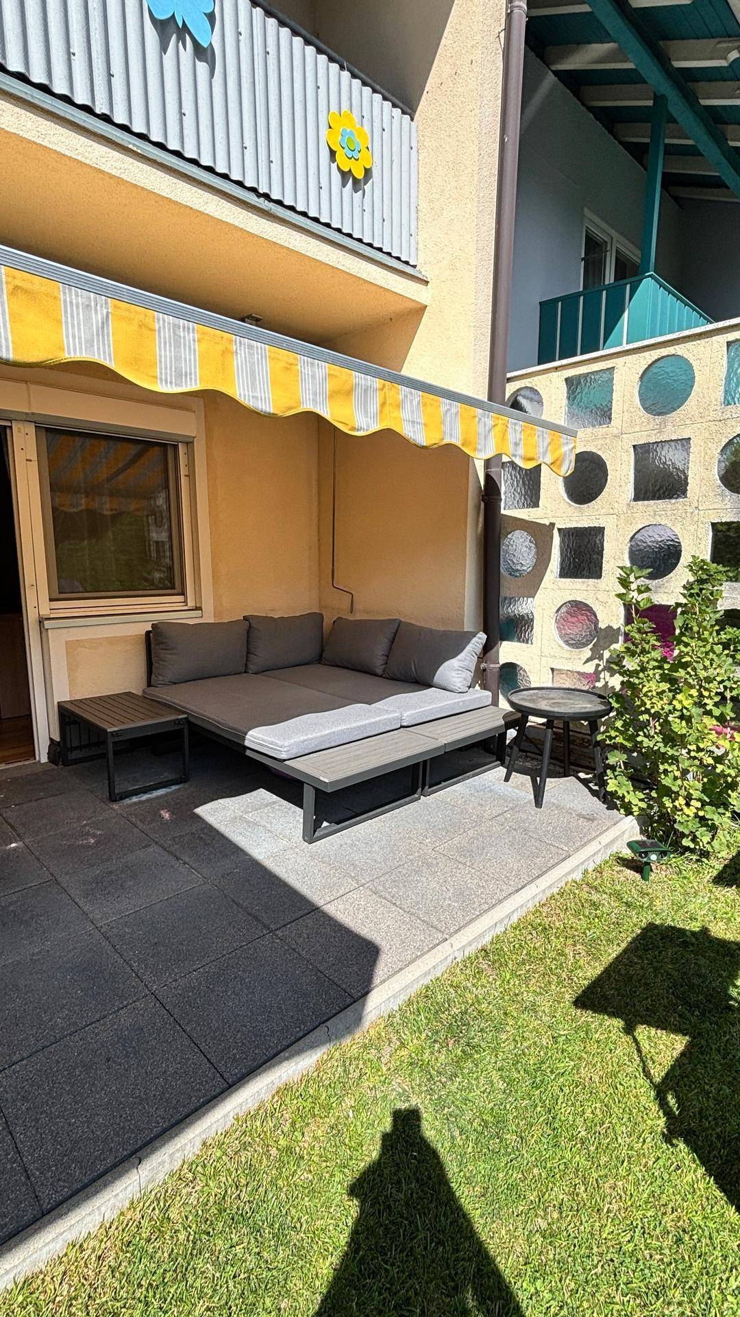 Gemütliche Terrasse mit Outdoor-Sofa, Markise und direktem Zugang zum grünen Garten.