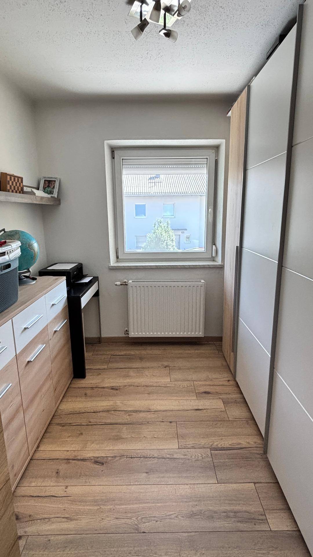Schmaler Raum mit Fenster, Heizkörper und praktischen Schränken, ideal als kleines Büro oder Ankleidezimmer.