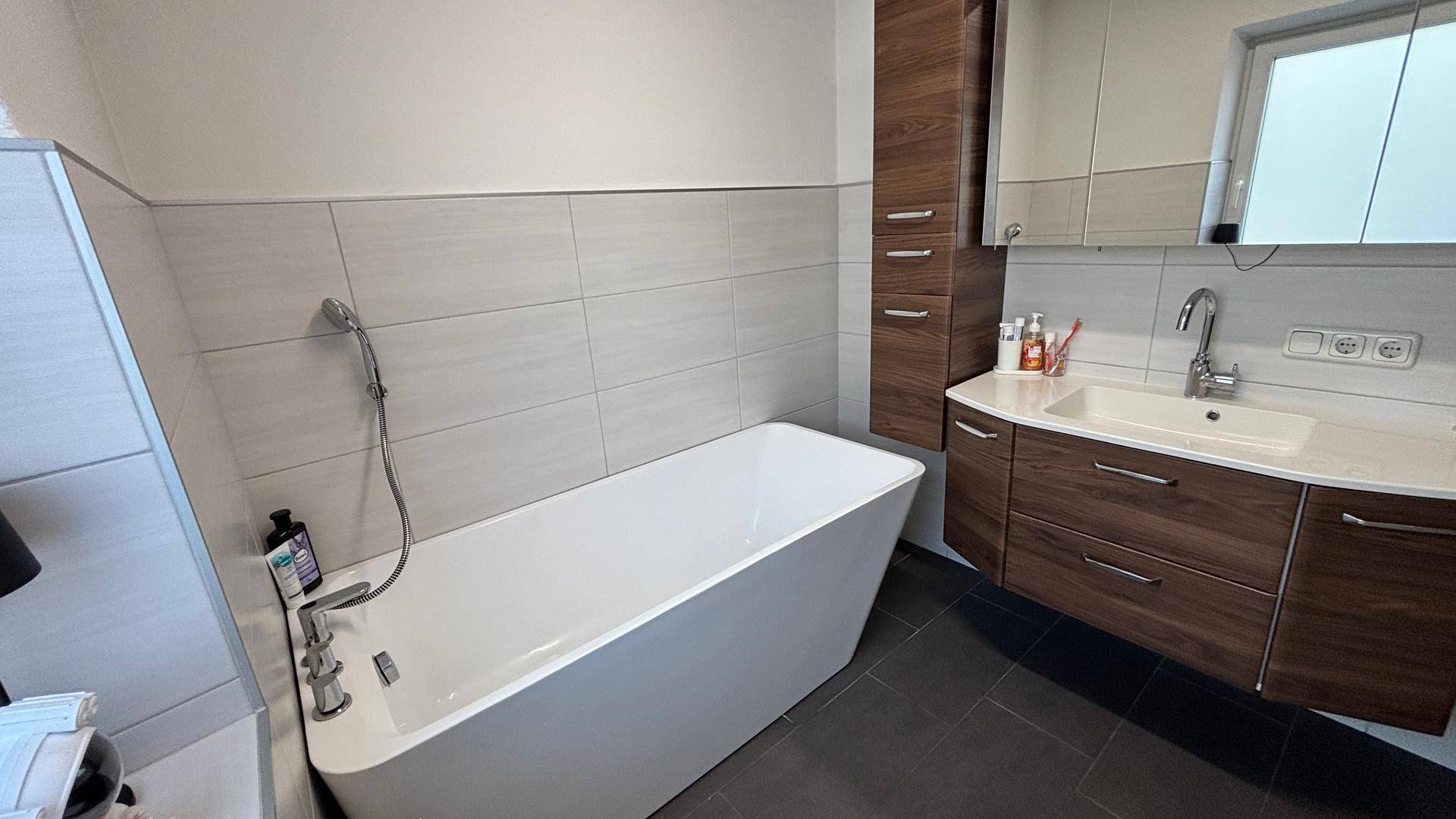 Modernes Badezimmer mit freistehender Badewanne, Holzwaschtisch und großem Spiegelschrank.
