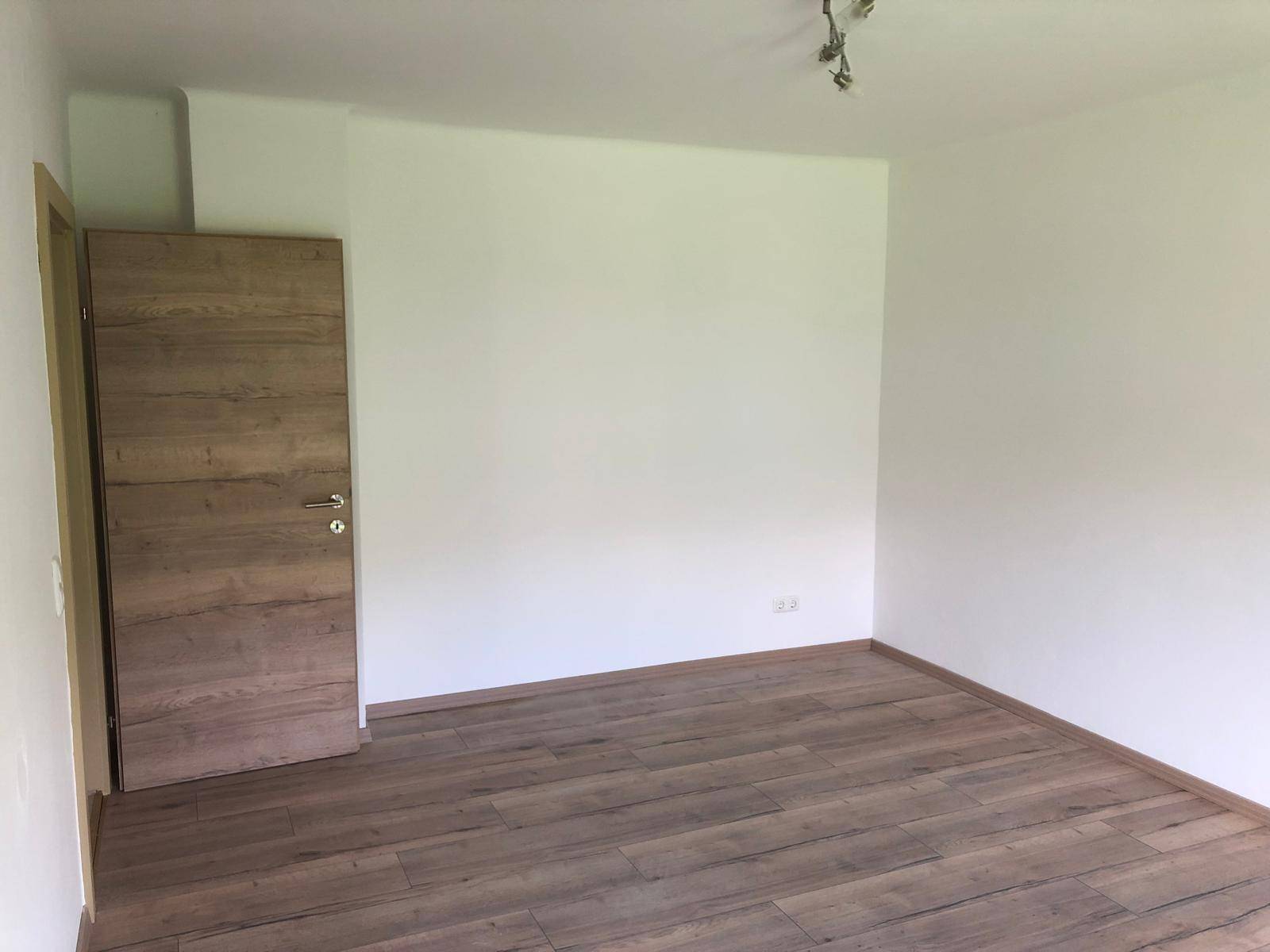 Leeres Zimmer mit weißen Wänden und Holzboden, bereit zur individuellen Gestaltung.