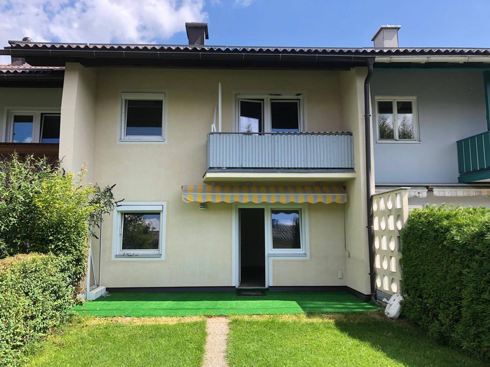 Rückansicht des Hauses mit Balkon, Terrasse und kleinem Gartenbereich unter blauem Himmel.