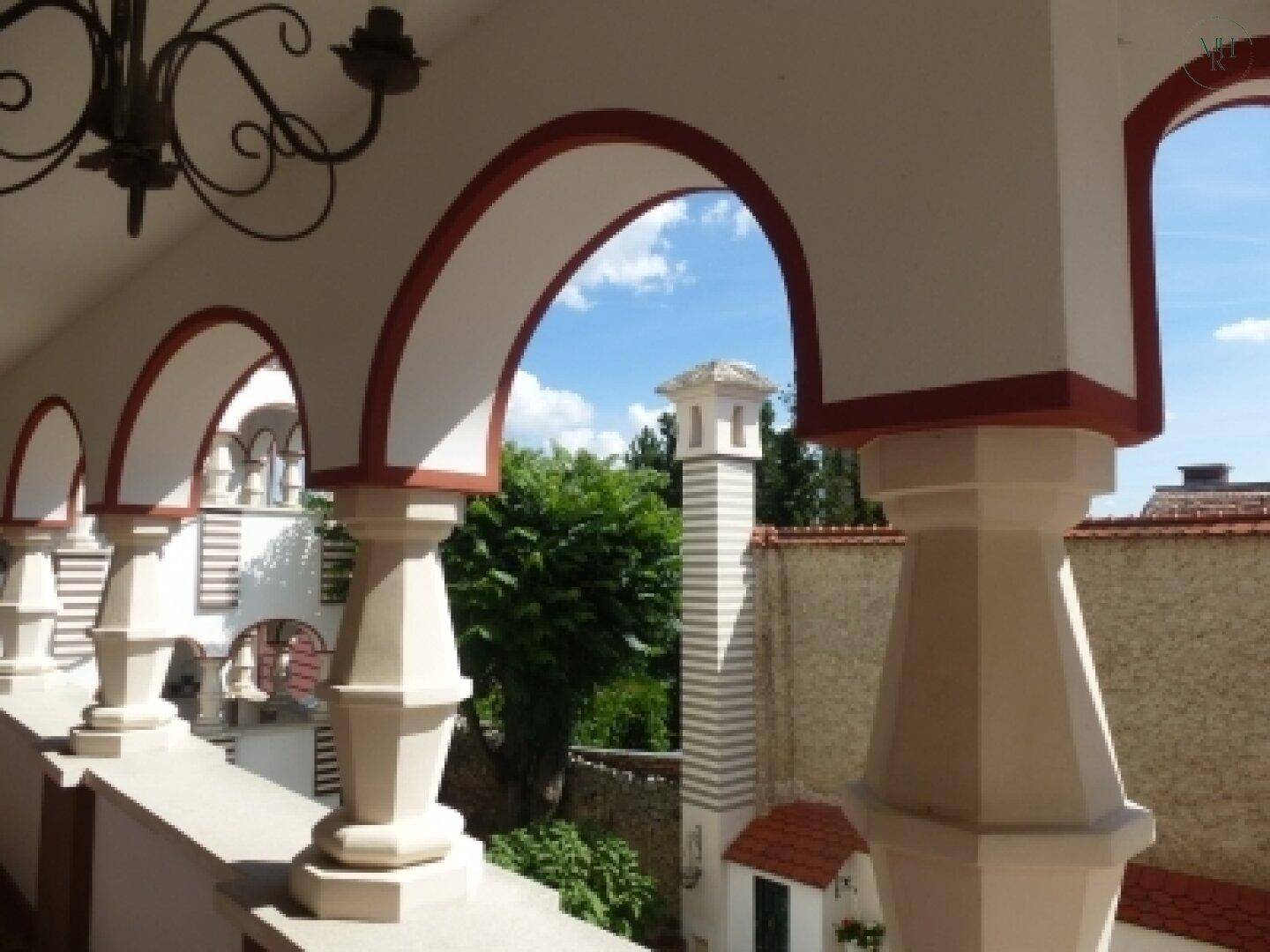 Blick von einem Bogenbalkon auf Bäume, einen Schornstein und die umliegende Landschaft.