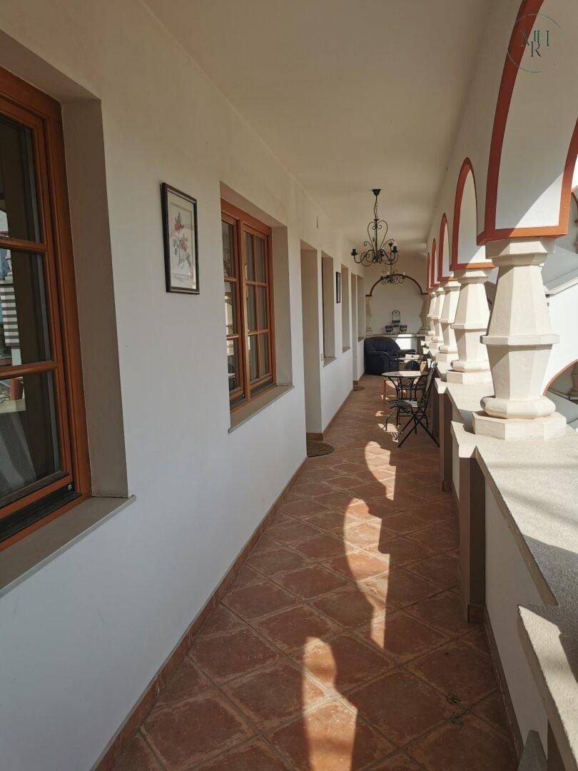 Langer überdachter Balkon mit Bögen, Terrakottafliesen und Sitzgelegenheiten im Freien.