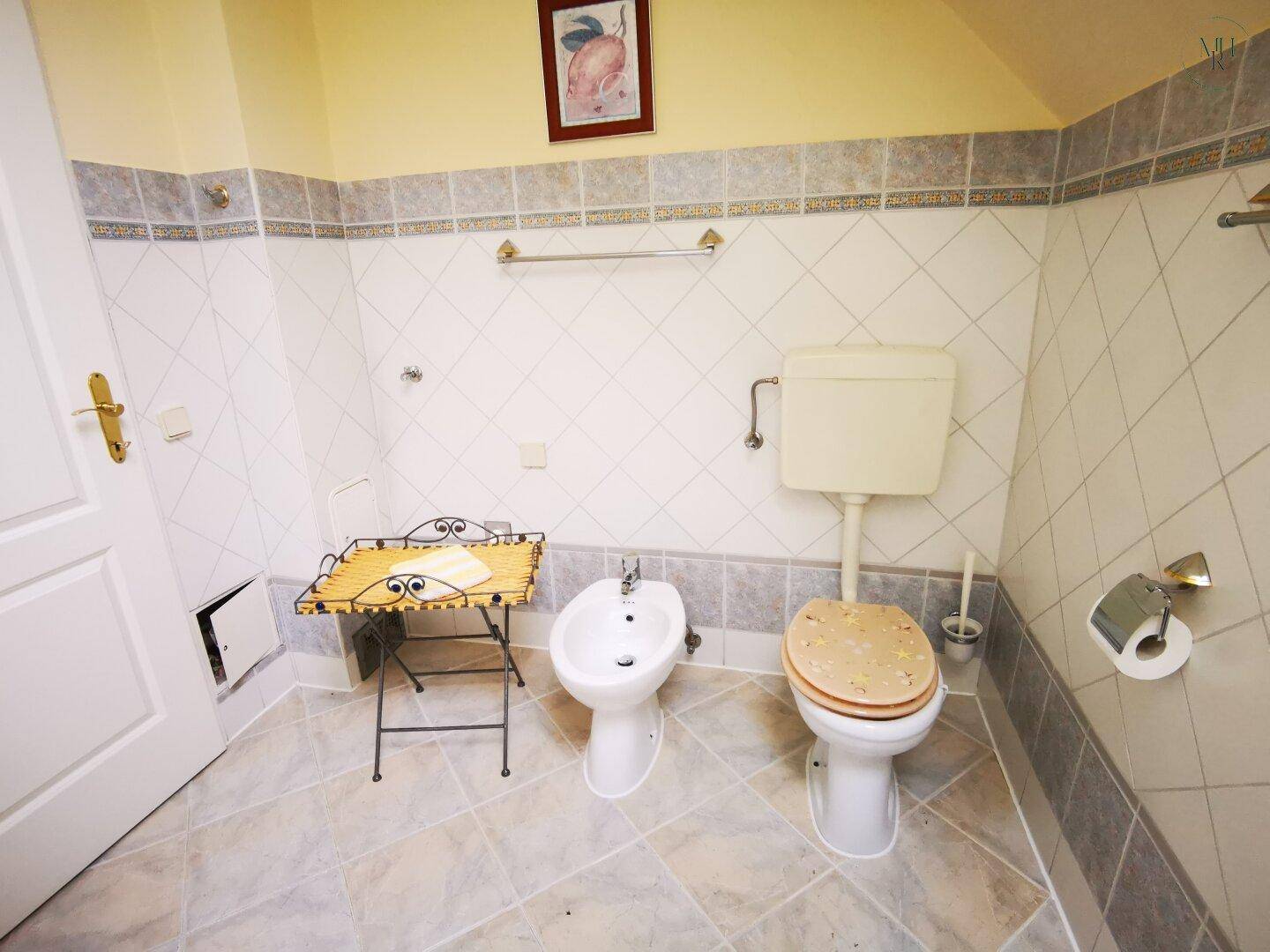 Badezimmer mit Toilette, Bidet und hellen Fliesen an Wänden und Boden.