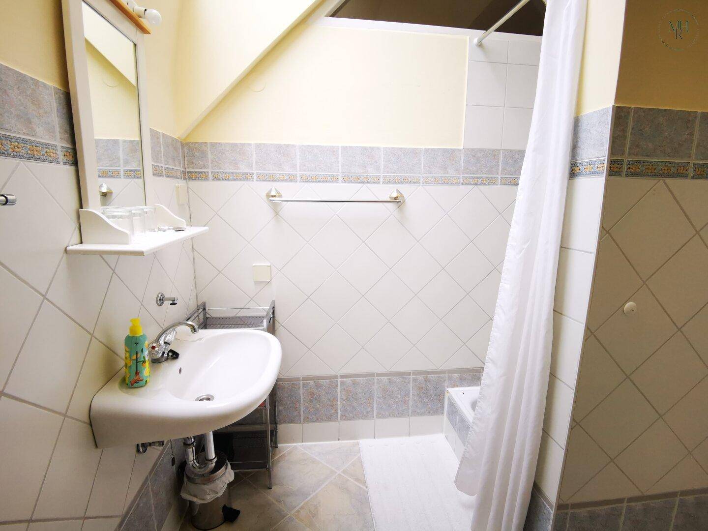 Badezimmer mit Waschbecken, Spiegel, Dusche und schrägen Wänden unter dem Dach.