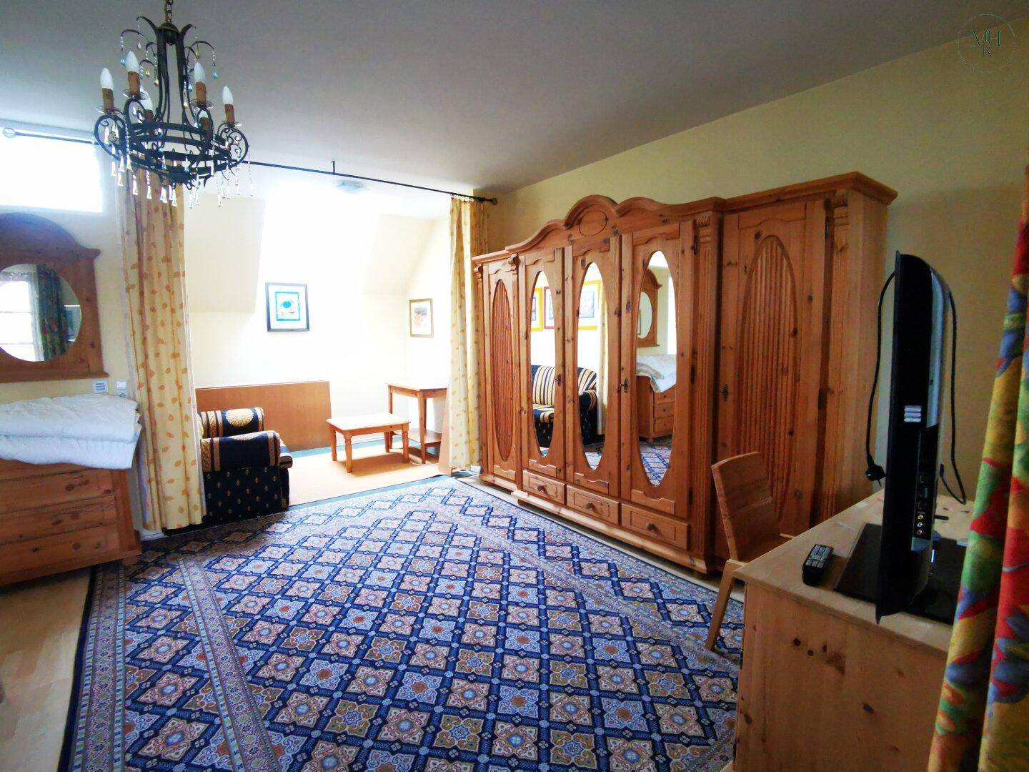 Helles Schlafzimmer mit Holzbett, großem Kleiderschrank, Teppich und gemütlicher Sitzecke.
