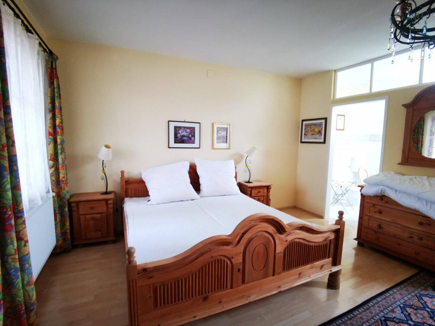 Gemütliches Schlafzimmer mit Holzbett, Nachttischen und Zugang zu einem sonnigen Außenbereich.