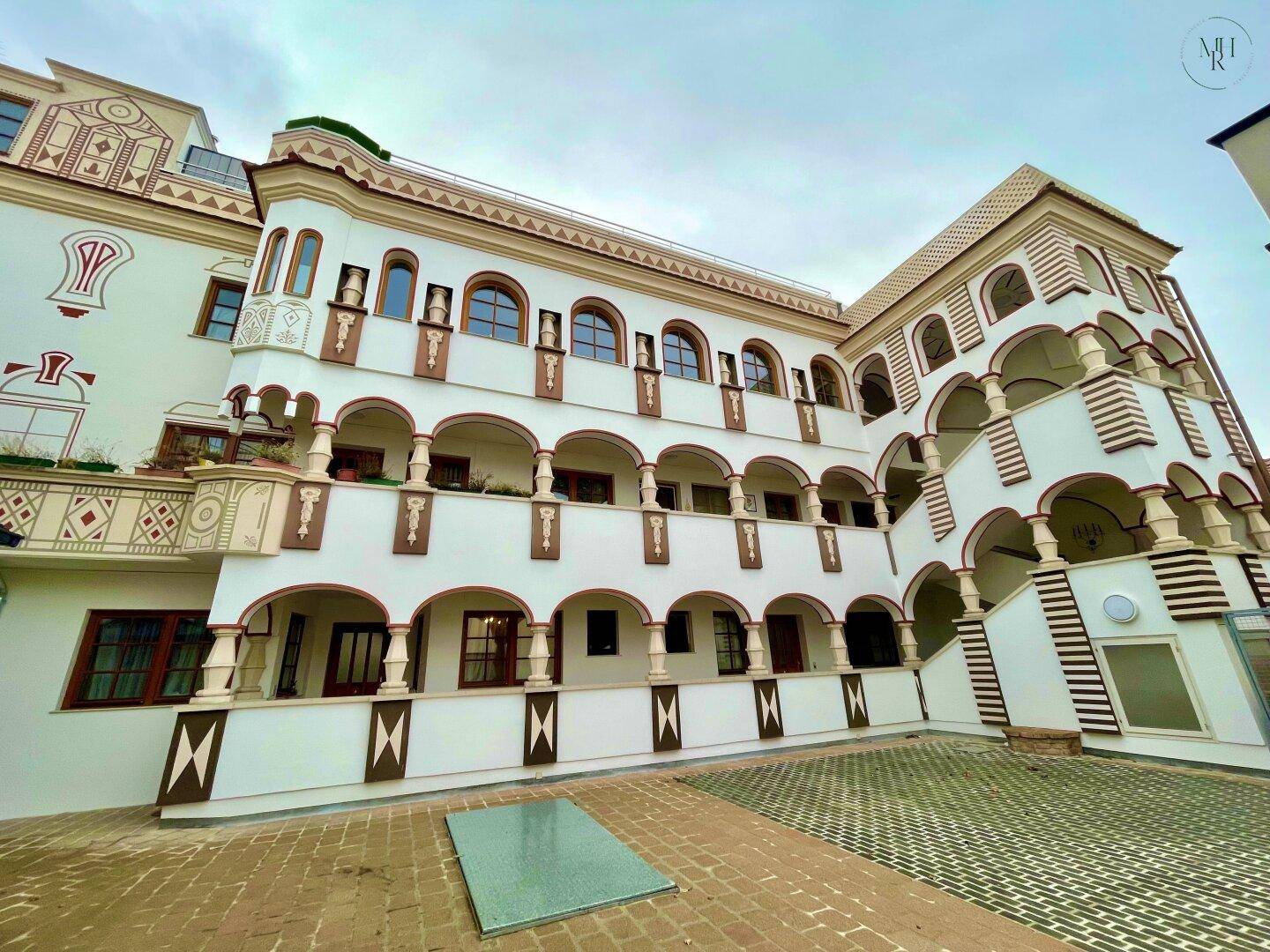 Ornate Fassade eines Gebäudes mit Bögen, Balkonen und einem gepflasterten Innenhof.