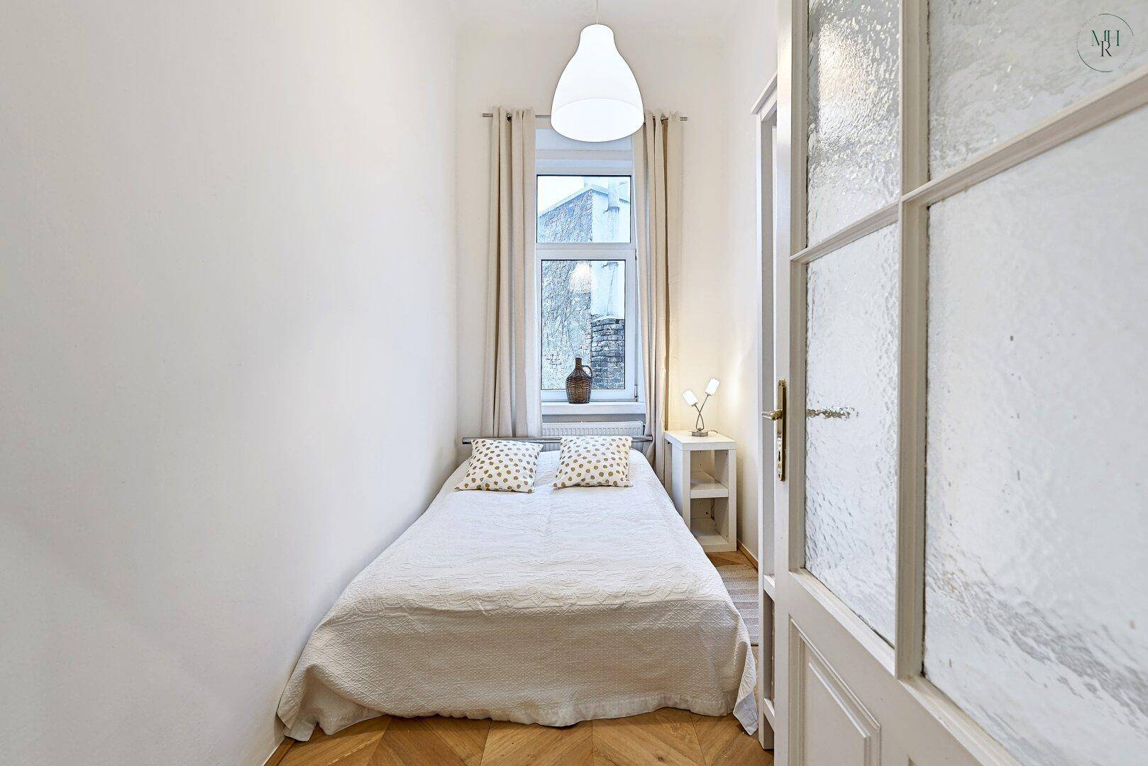 Kleines, helles Schlafzimmer mit Einzelbett, Parkettboden und Fensterblick.