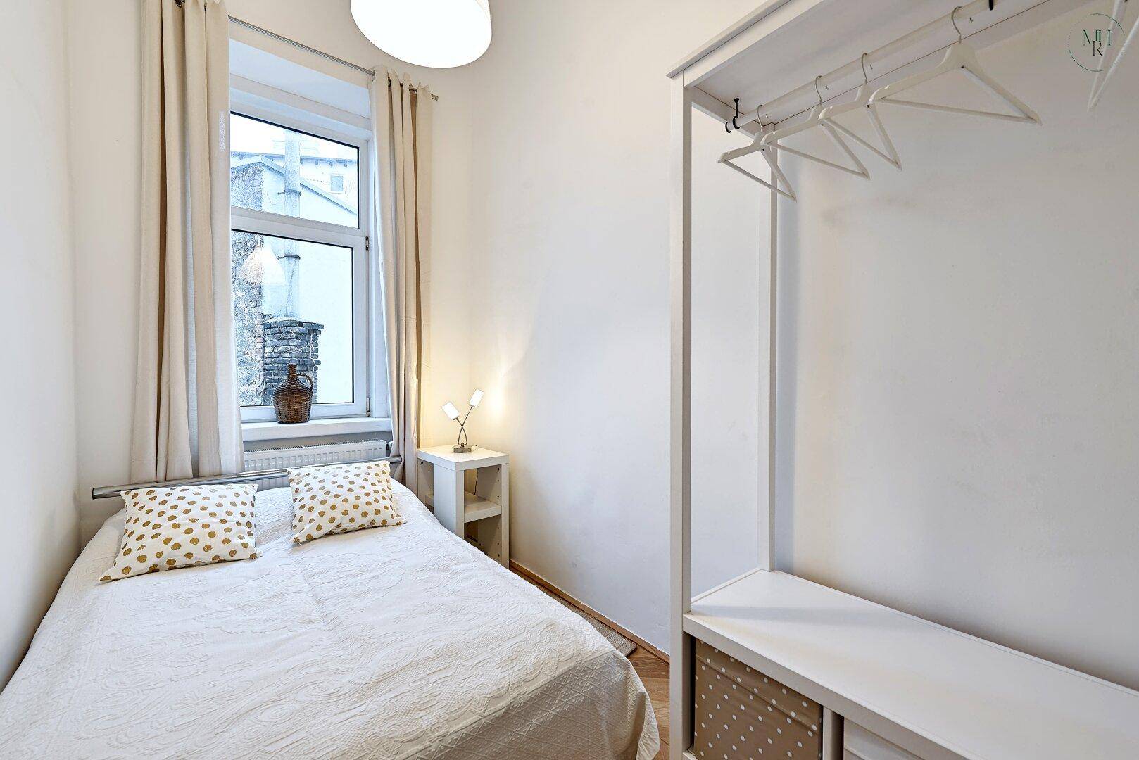 Helles Schlafzimmer mit Einzelbett, offenem Kleiderschrank und Fenster.