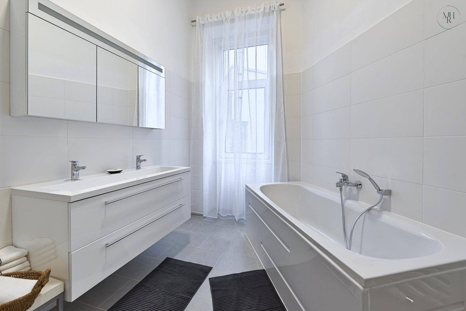 Modernes Badezimmer mit Doppelwaschbecken, Badewanne und Fenster für Tageslicht.