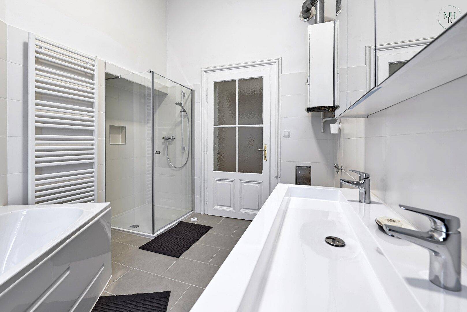 Helles Badezimmer mit Dusche, Waschtisch und beheiztem Handtuchhalter.