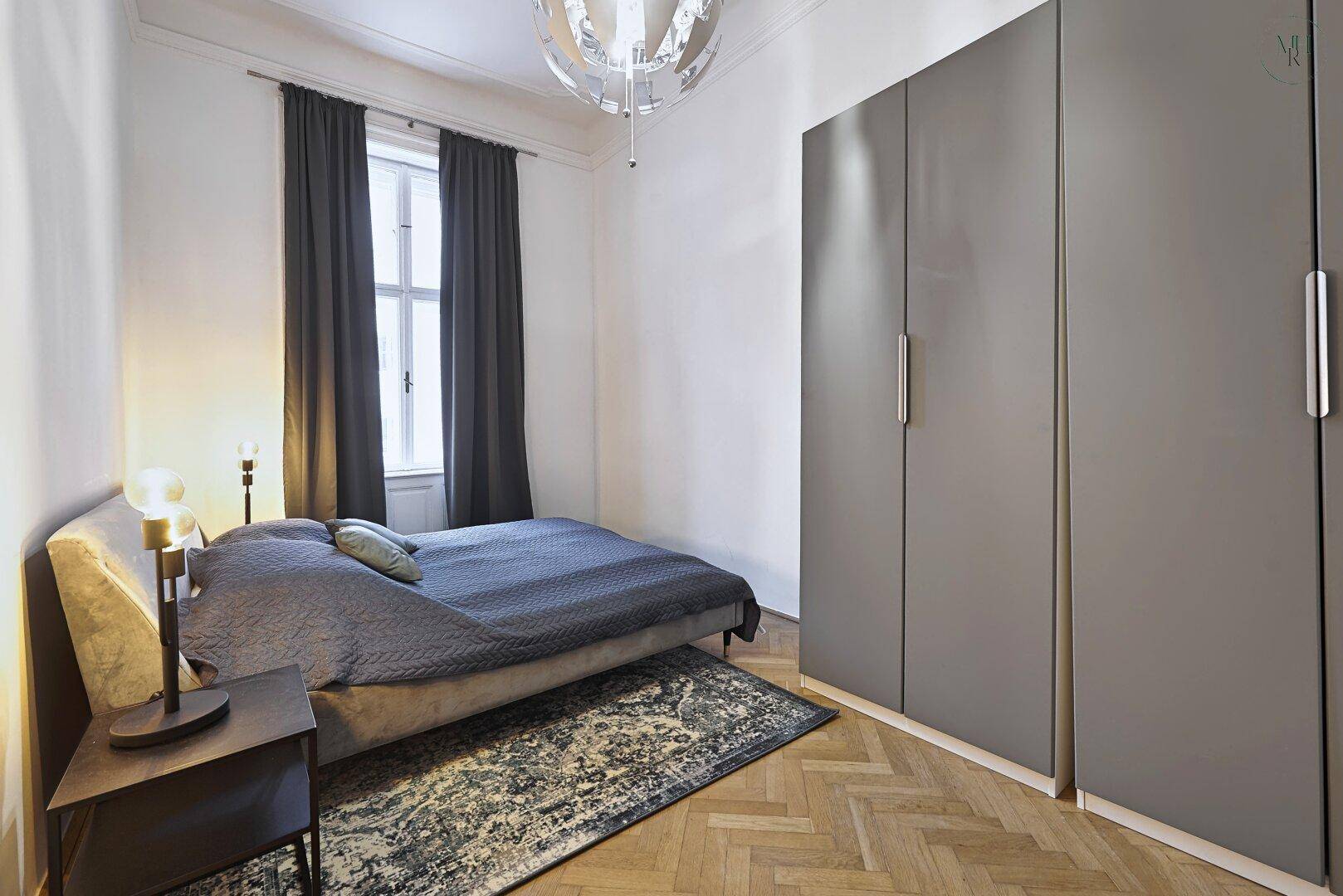 Schlafzimmer mit Doppelbett, grauen Einbauschränken und Parkettboden.