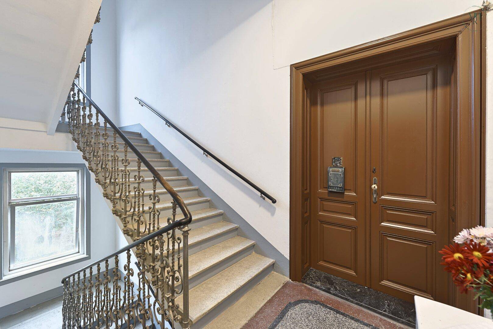 Historisches Treppenhaus mit schmiedeeisernem Geländer und Holztüren.