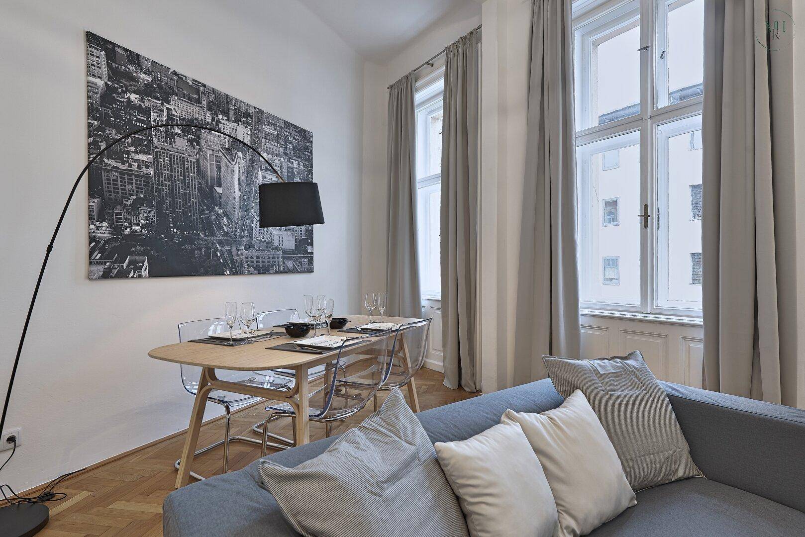 Heller Wohn-Essbereich mit Esstisch, Sofa und großen Fenstern.
