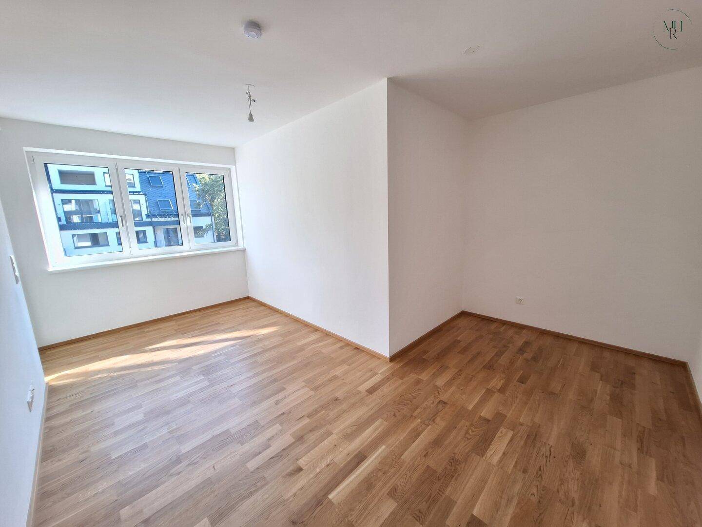 Helles Schlafzimmer mit Holzparkettboden und großem Fenster, bietet viel Tageslicht und Ausblick.