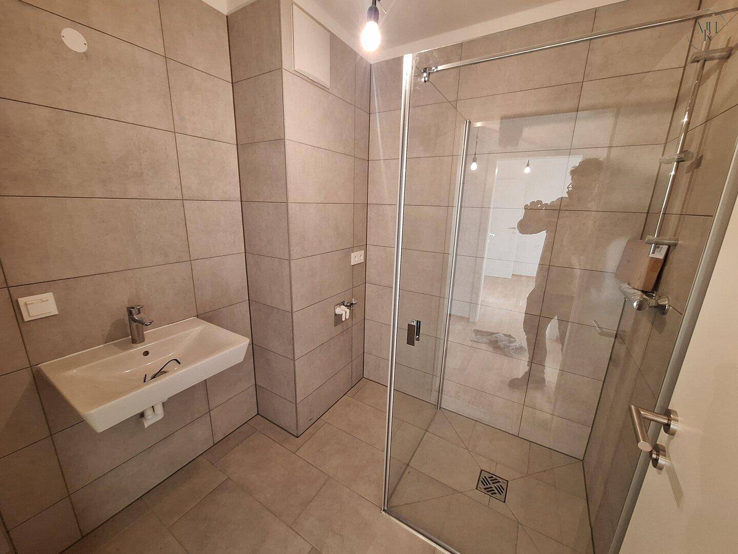 Modernes Badezimmer mit begehbarer Dusche, Fliesenboden und Wandfliesen in neutralem Grau.