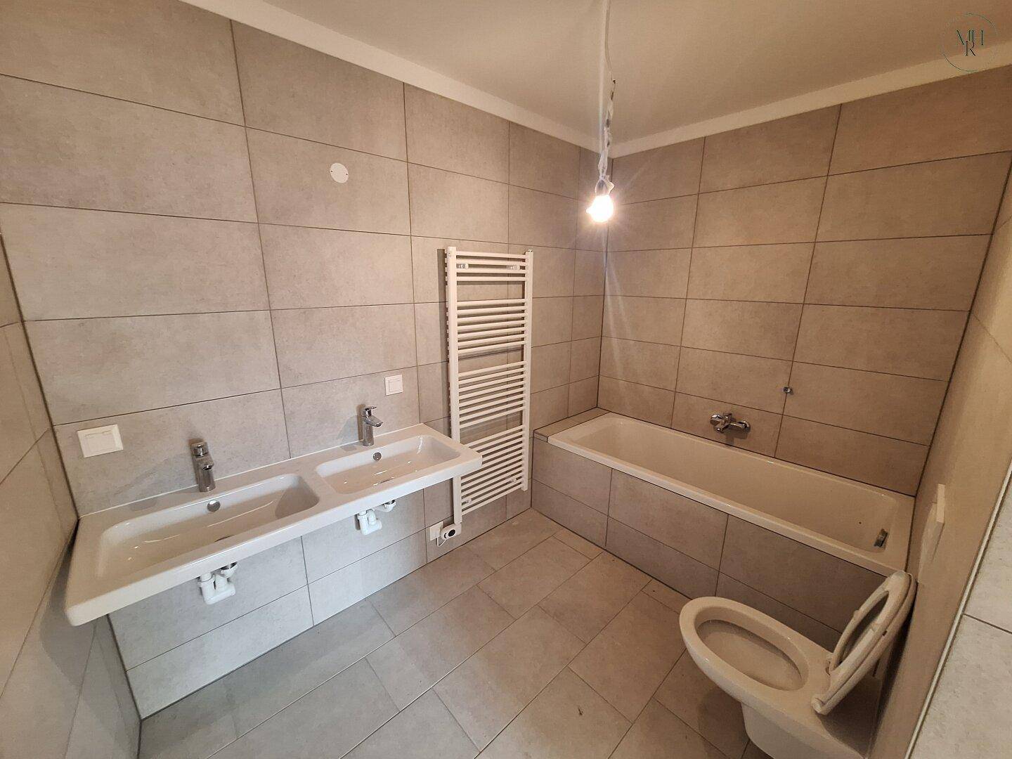 Geräumiges Badezimmer mit Badewanne, Doppelwaschbecken und beheiztem Handtuchhalter.