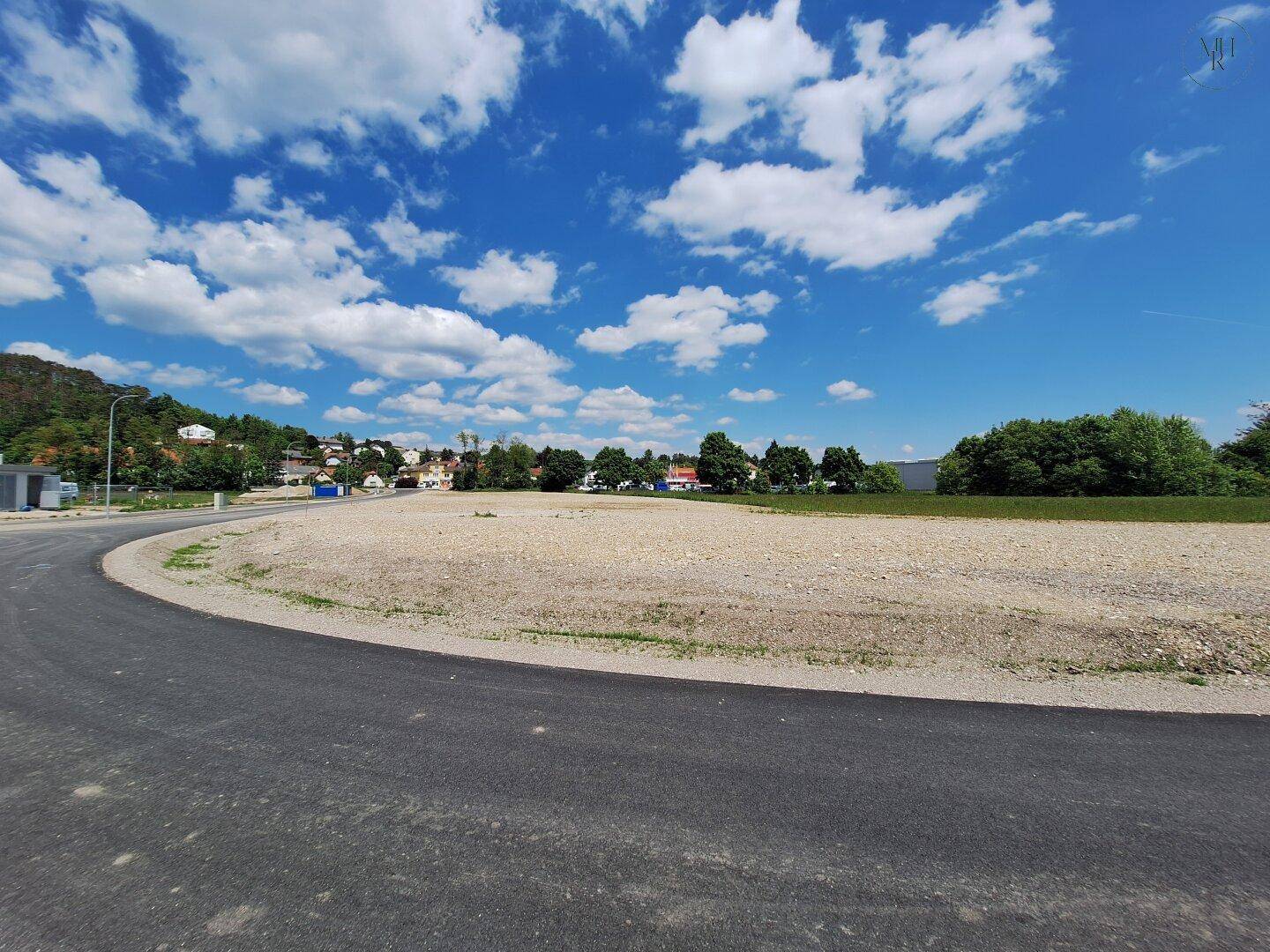 Unbebautes Baugrundstück mit frischer Asphaltstraße und Panoramablick auf die Hügellandschaft.