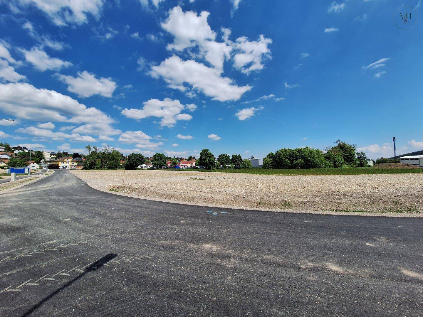 Weitläufiges unbebautes Areal mit neuem Straßenabschnitt und Blick auf die grüne Umgebung.