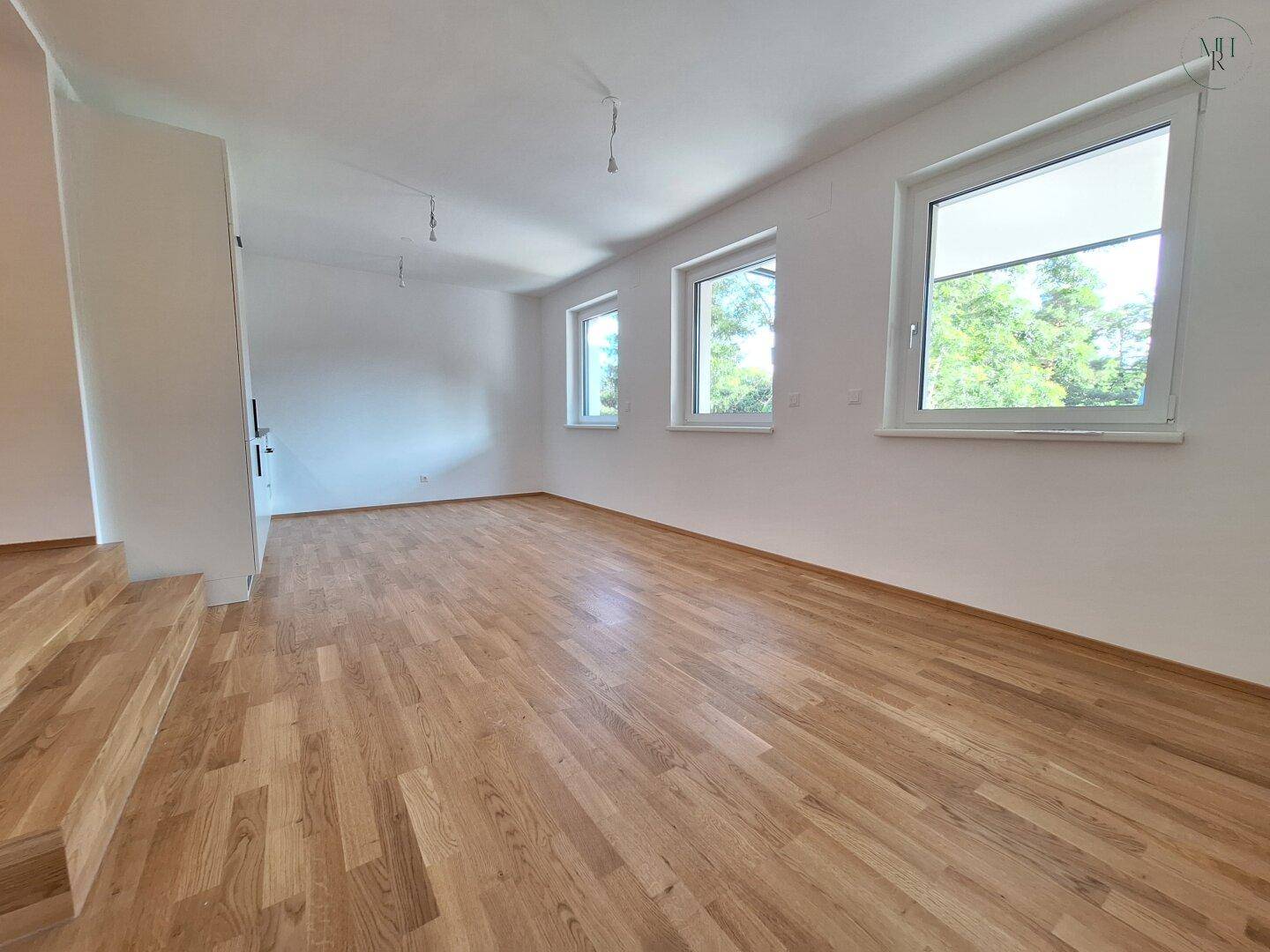 Geräumiger, heller Raum mit Eichenparkett und drei großen Fenstern, ideal als Wohnzimmer.