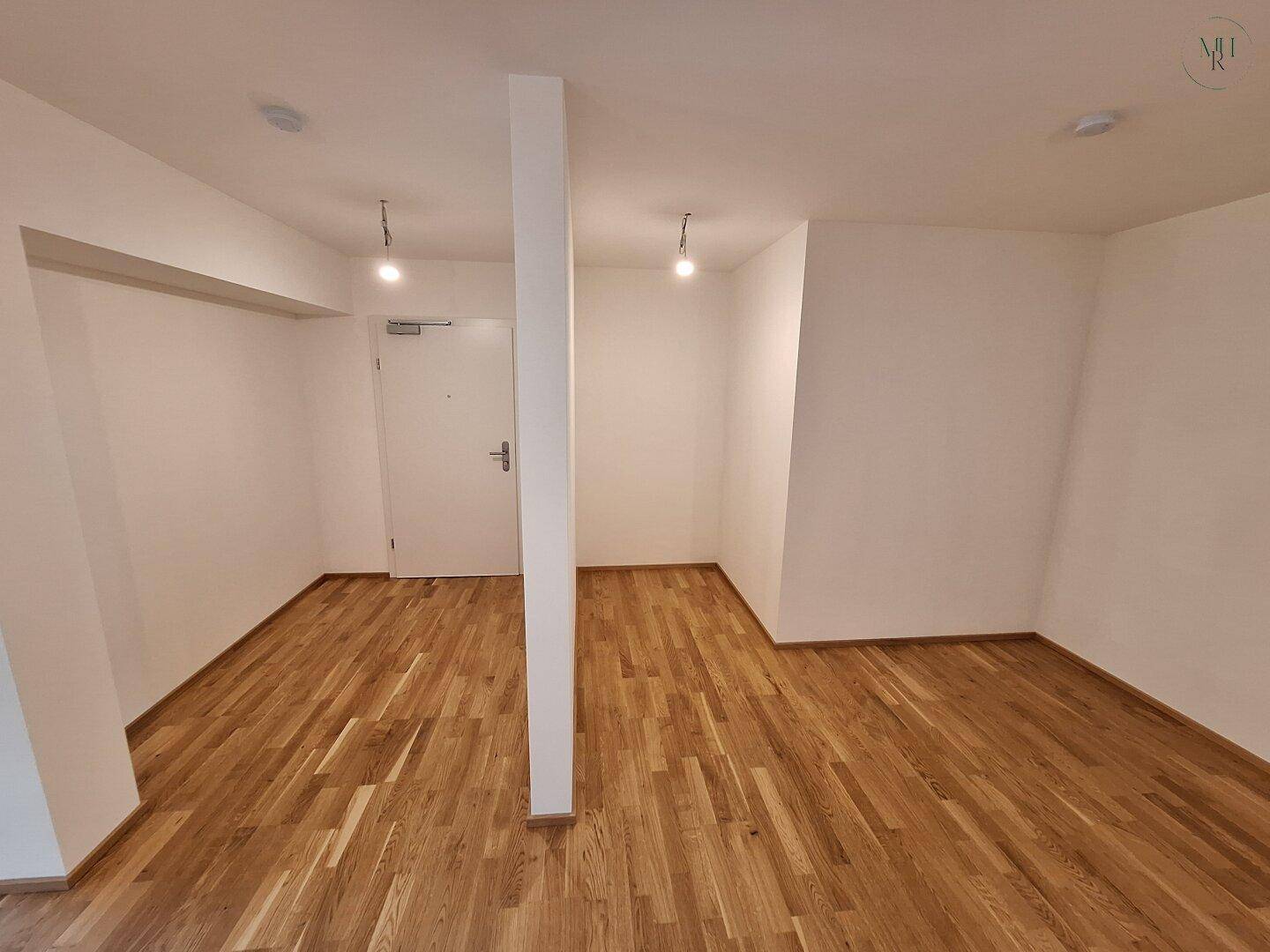 Heller Eingangsbereich mit Holzparkett und weiß gestrichenen Wänden, bereit zur individuellen Gestaltung.
