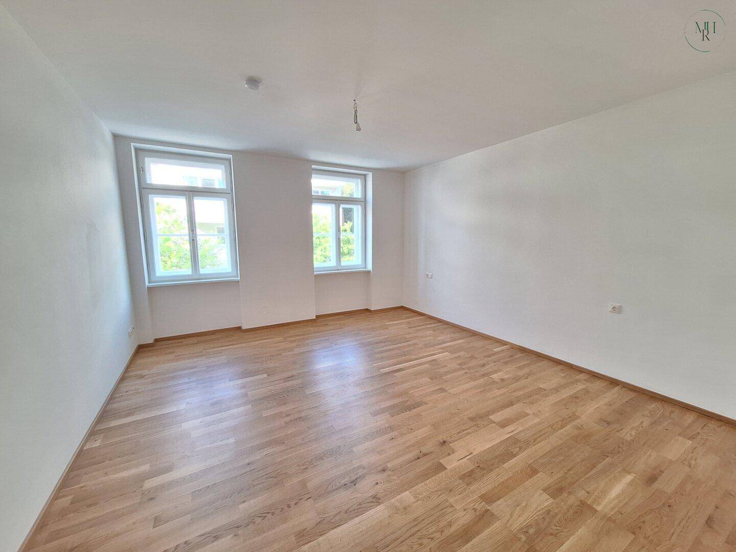 Helles Schlafzimmer mit Parkettboden und zwei Fenstern, die eine angenehme Atmosphäre schaffen.