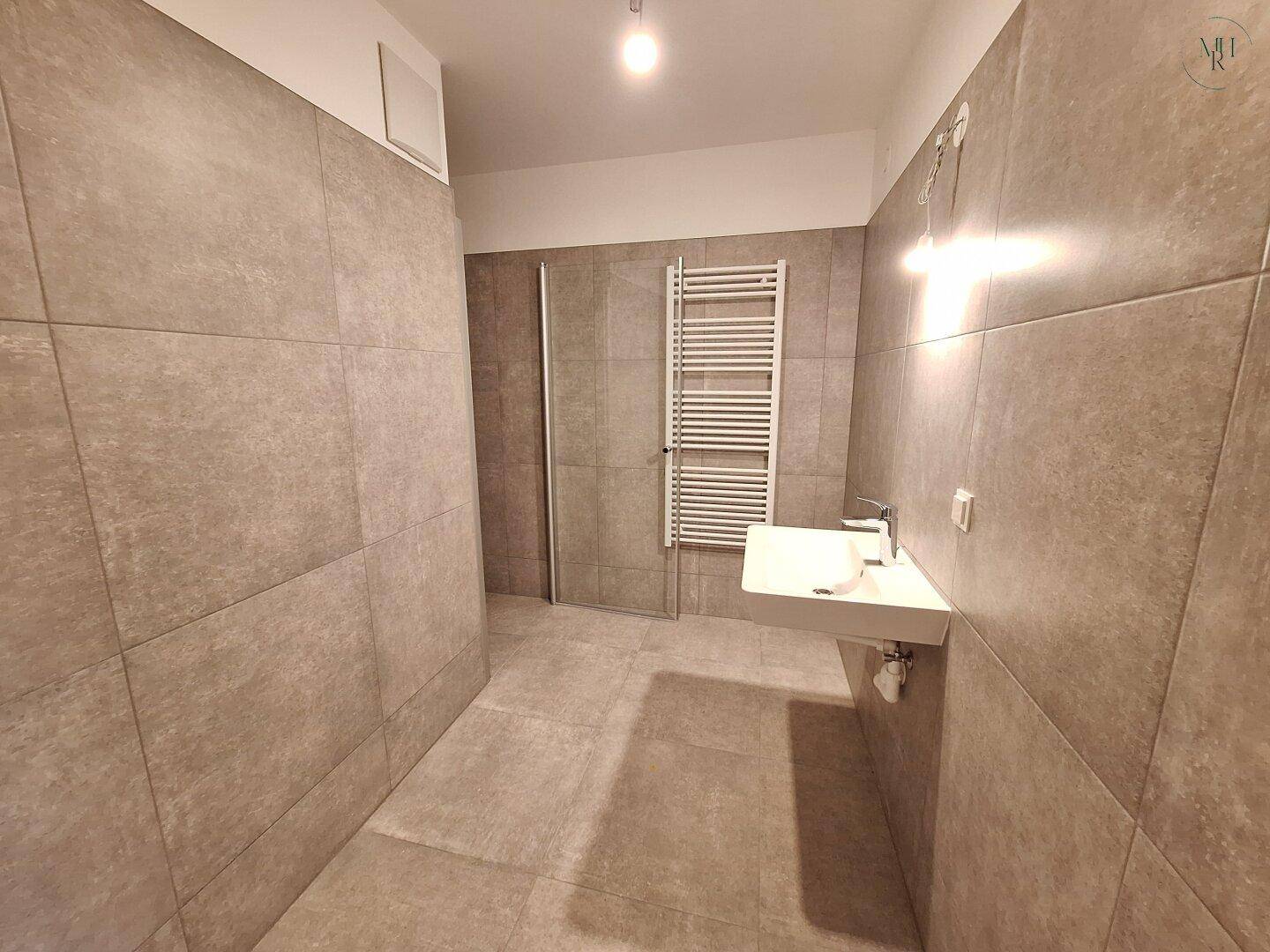Modernes Badezimmer mit grauen Fliesen, Einzelwaschbecken, beheiztem Handtuchhalter und begehbarer Dusche.