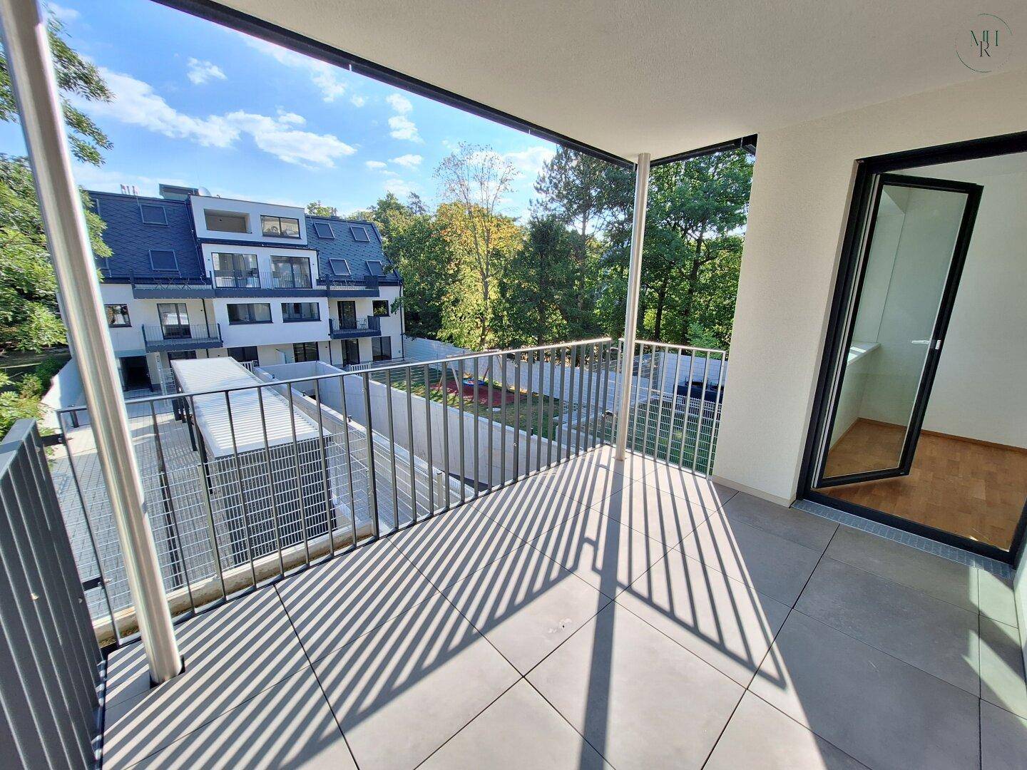 Sonniger Balkon mit modernem Fliesenboden und Blick auf ein neues Gebäude und Bäume.