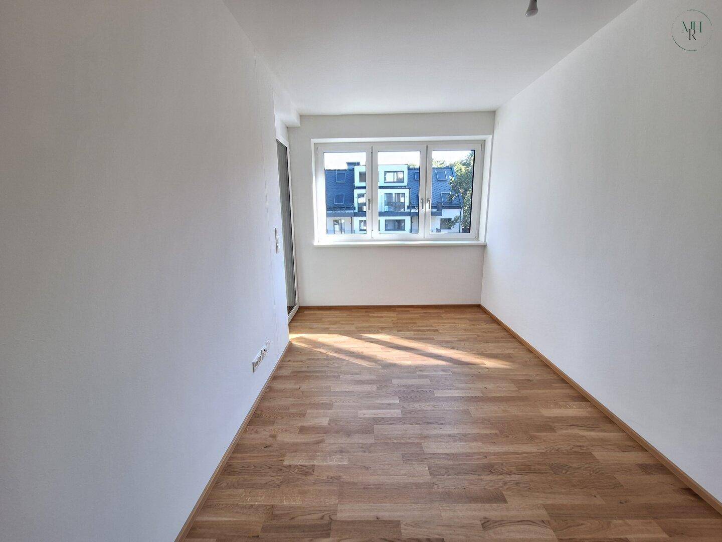Langes, helles Zimmer mit Parkettboden und großem Fenster, das viel Tageslicht spendet.