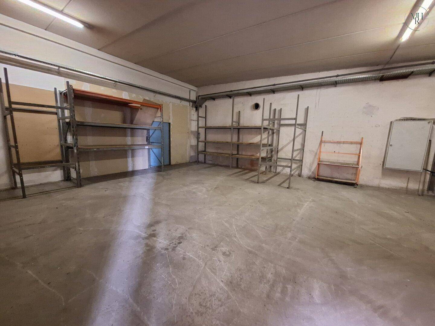 Geräumiger Lagerbereich mit Betonboden und mehreren Metallregalen für die effiziente Lagerung von Gütern.