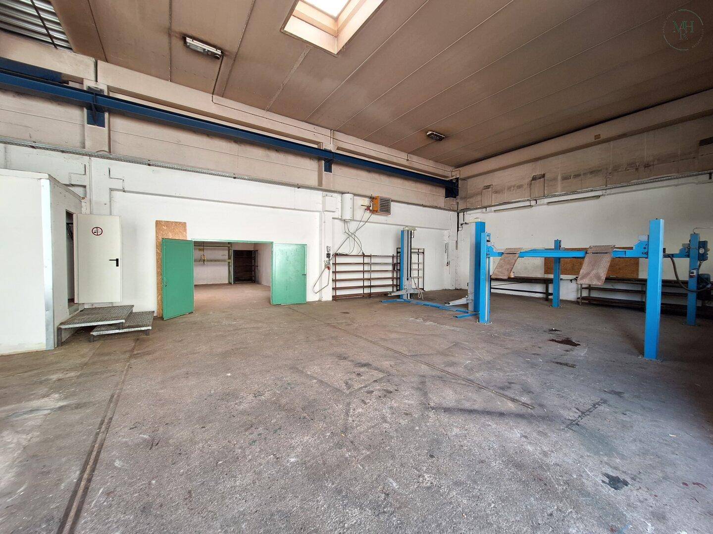Große Werkstatthalle mit Betonboden, Oberlicht und einem blauen Fahrzeuglift, bereit für Reparaturen.