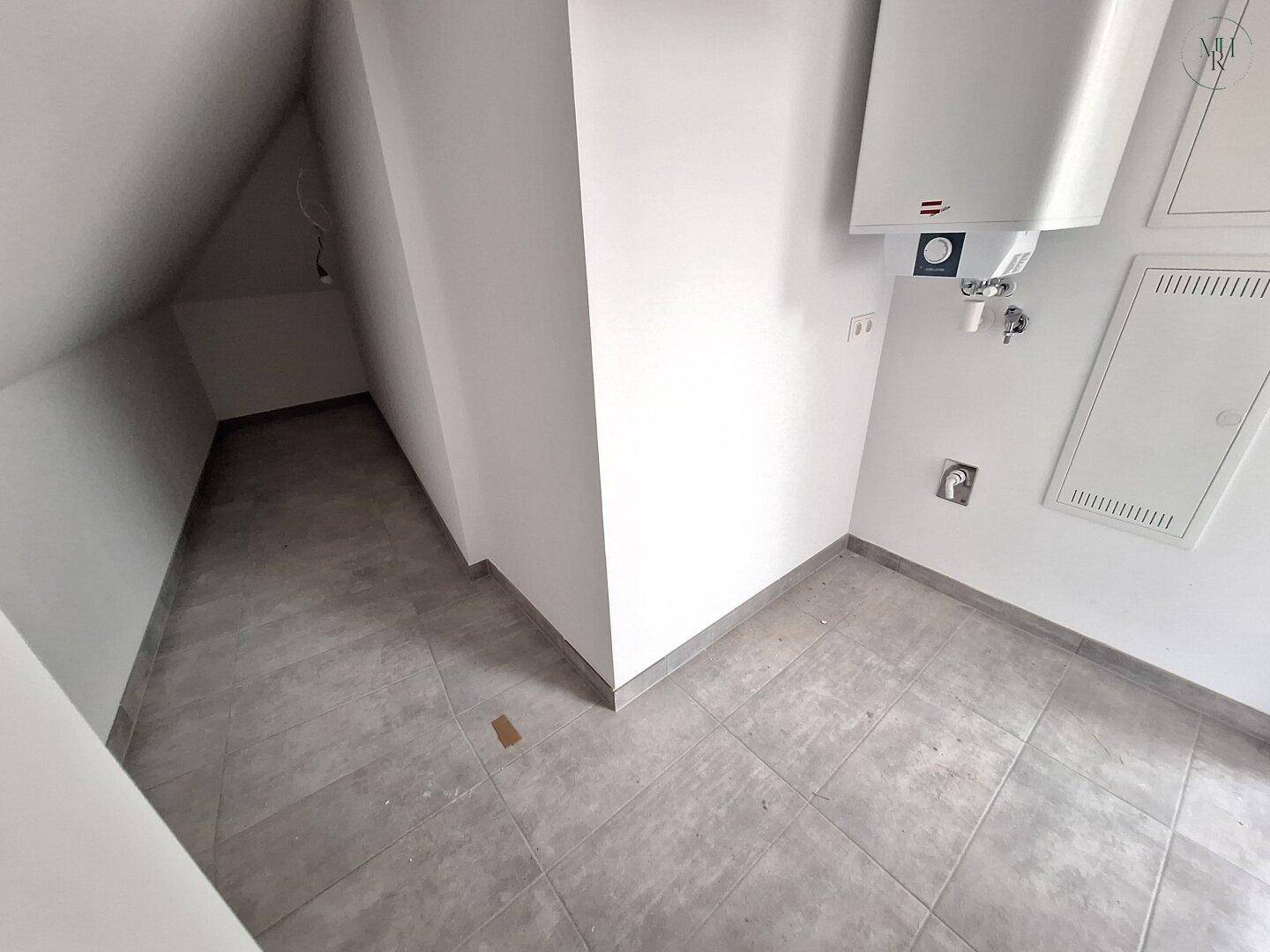 Praktischer Hauswirtschaftsraum mit Fliesenboden, Dachschräge und Warmwasserbereiter.