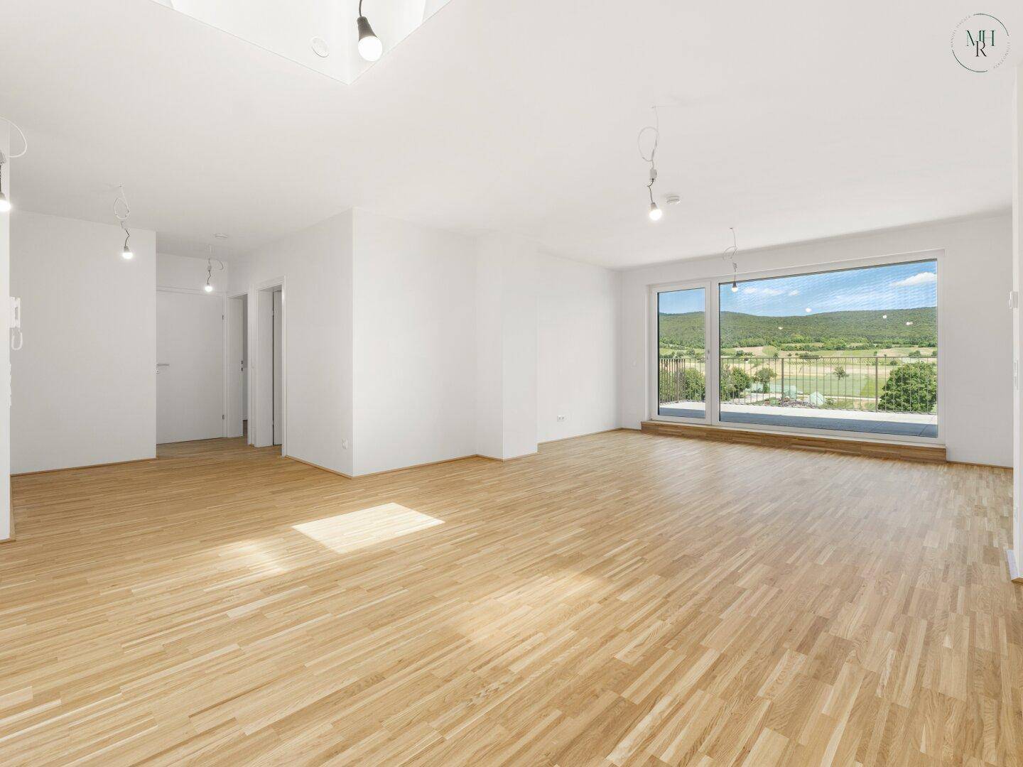 Heller, leerer Wohnraum mit Holzboden und großen Fenstern, die einen weiten Blick ins Grüne bieten.