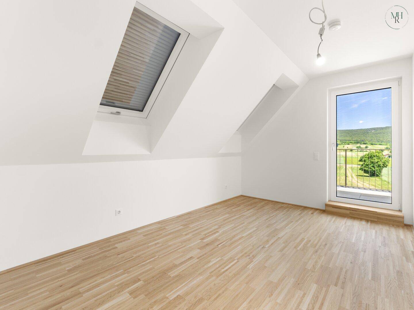 Dachgeschosszimmer mit Holzboden, Dachschrägen, Oberlicht und Zugang zu einem Balkon.
